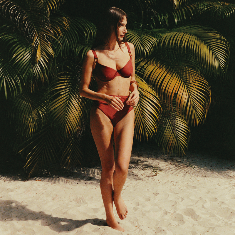 Woman in a red bikini standing on a sandy beach with palm leaves in the background