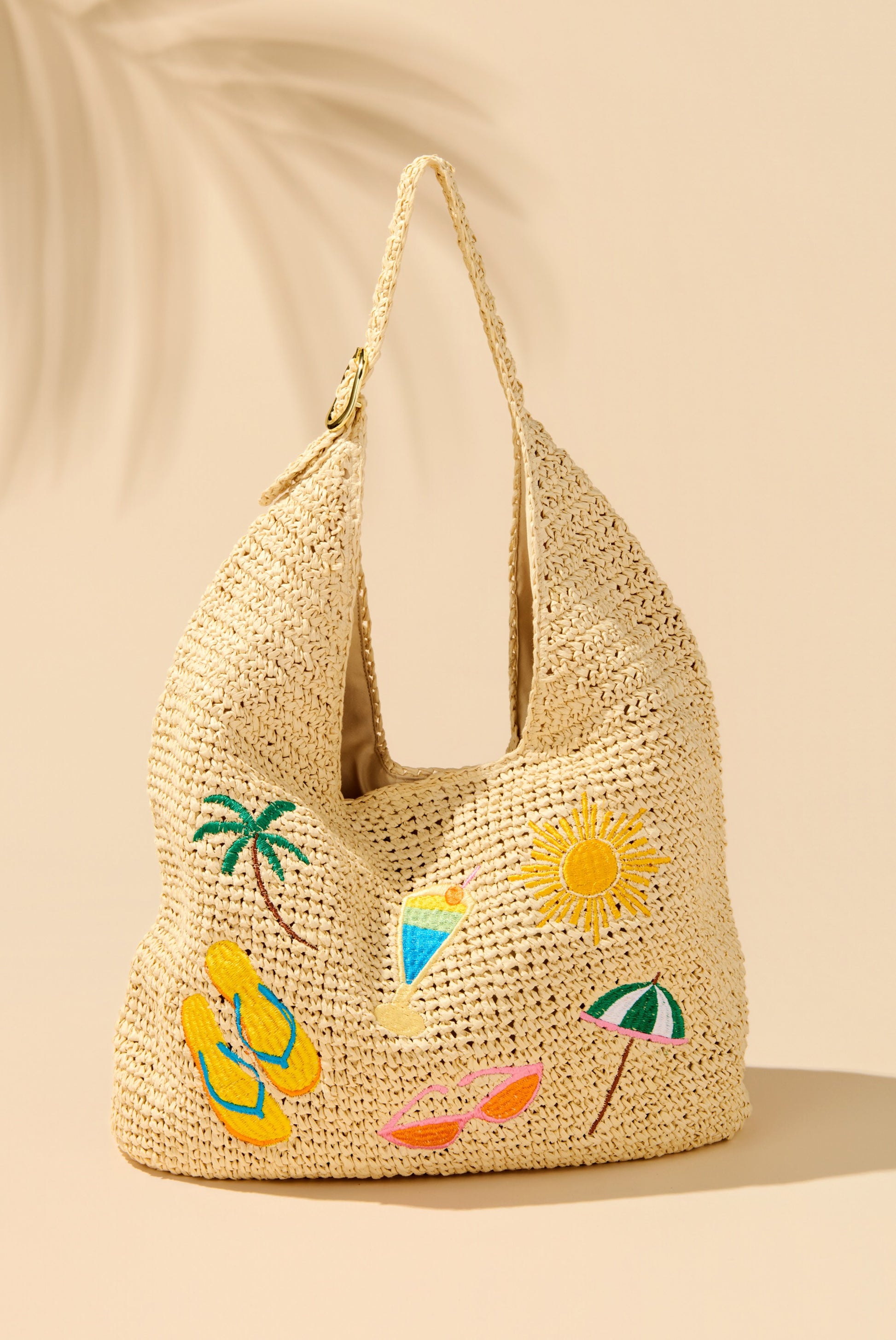 The Cabana Slouchy Tote by South Moon Under features embroidered palm tree, sun, cocktail, yellow flip-flops, pink sunglasses, and a beach umbrella on a Tan Multi woven straw bag—perfect for tropical flair.