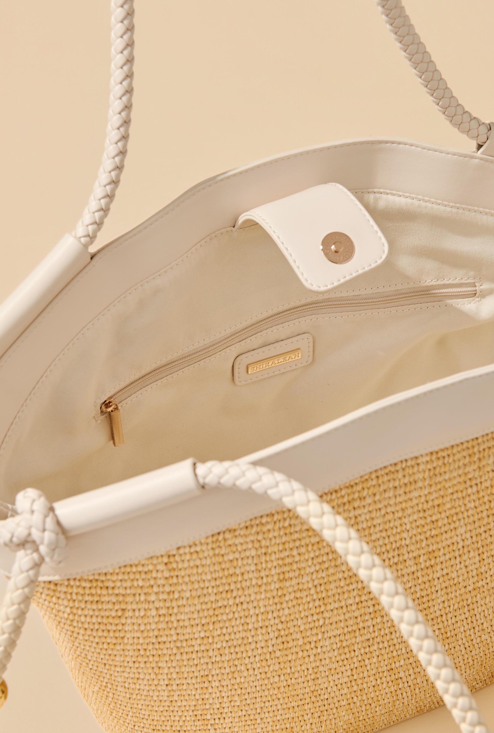 A close-up of the Gina Tote by South Moon Under—a spacious woven bag with white faux leather trim and handles, showcasing its cream interior, zipper pocket, and snap closure.