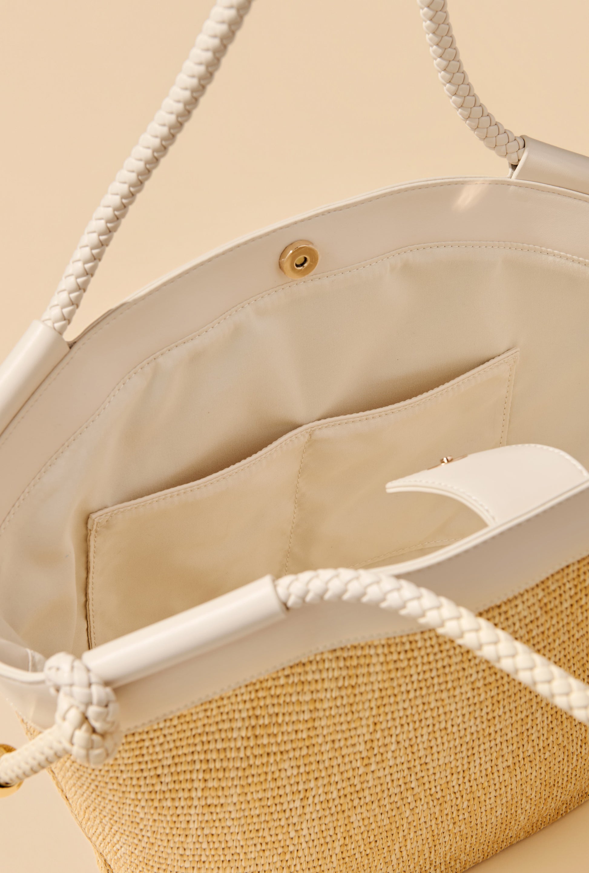 Close-up of the Gina Tote by South Moon Under, featuring white faux leather trim, braided handles, a beige fabric interior with an inner pocket, and a magnetic snap closure.