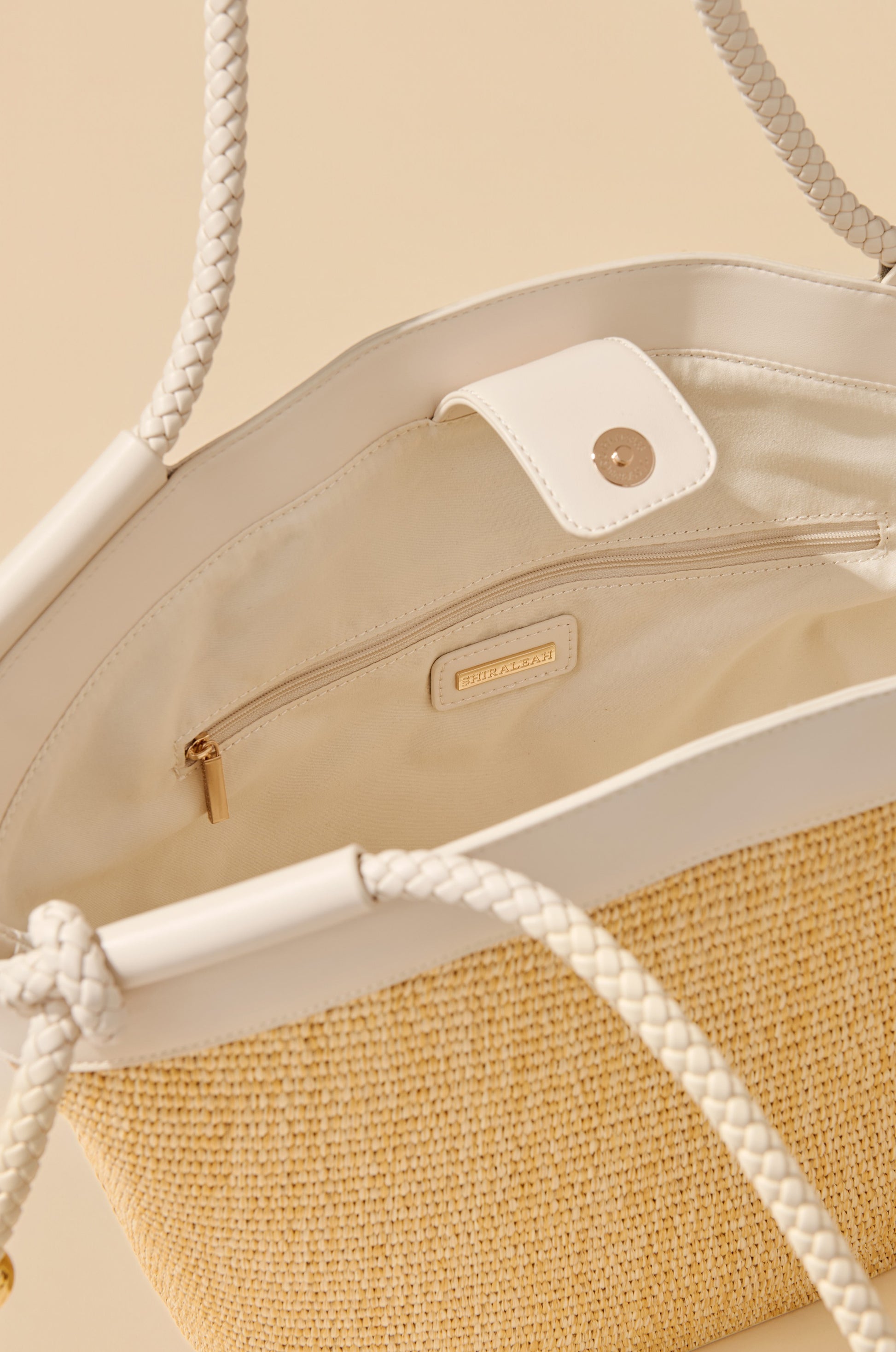 A close-up of the South Moon Under Gina Tote, a beige woven tote with white faux leather trim, braided handles, fabric lining, interior zip pocket, and magnetic snap closure.