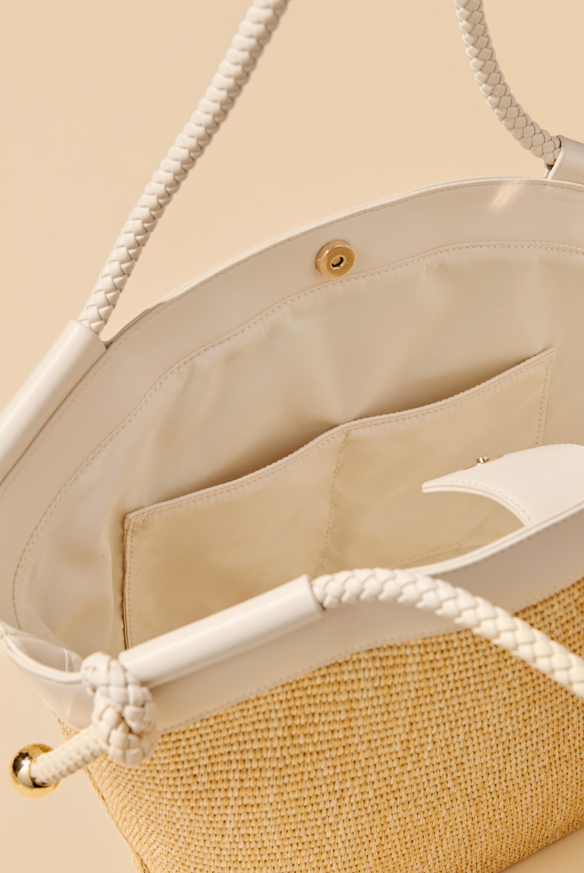 Close-up of the Gina Tote by South Moon Under, a woven bag with white faux leather trim, braided handles, gold hardware, an inner pocket with snap closure, and cream fabric lining.