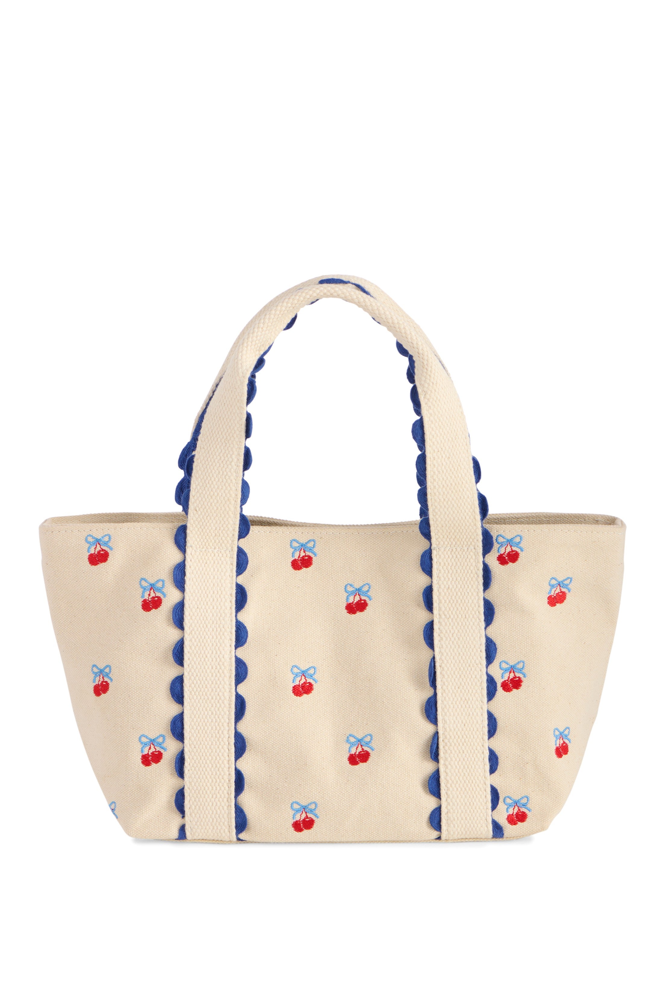 The South Moon Under Cherry Icon Mini Tote is a beige canvas bag with blue scalloped handle trim, decorated with small embroidered cherry and blue bow designs across its surface.