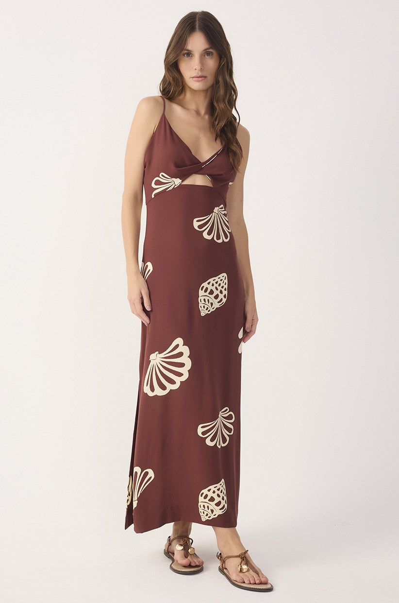 A woman wears the Dress To Brown Maritime Cut-out Smocked Maxi Dress with adjustable spaghetti straps, seashell print, V-neckline, front cut-out, paired with flat metallic sandals and long wavy brown hair.