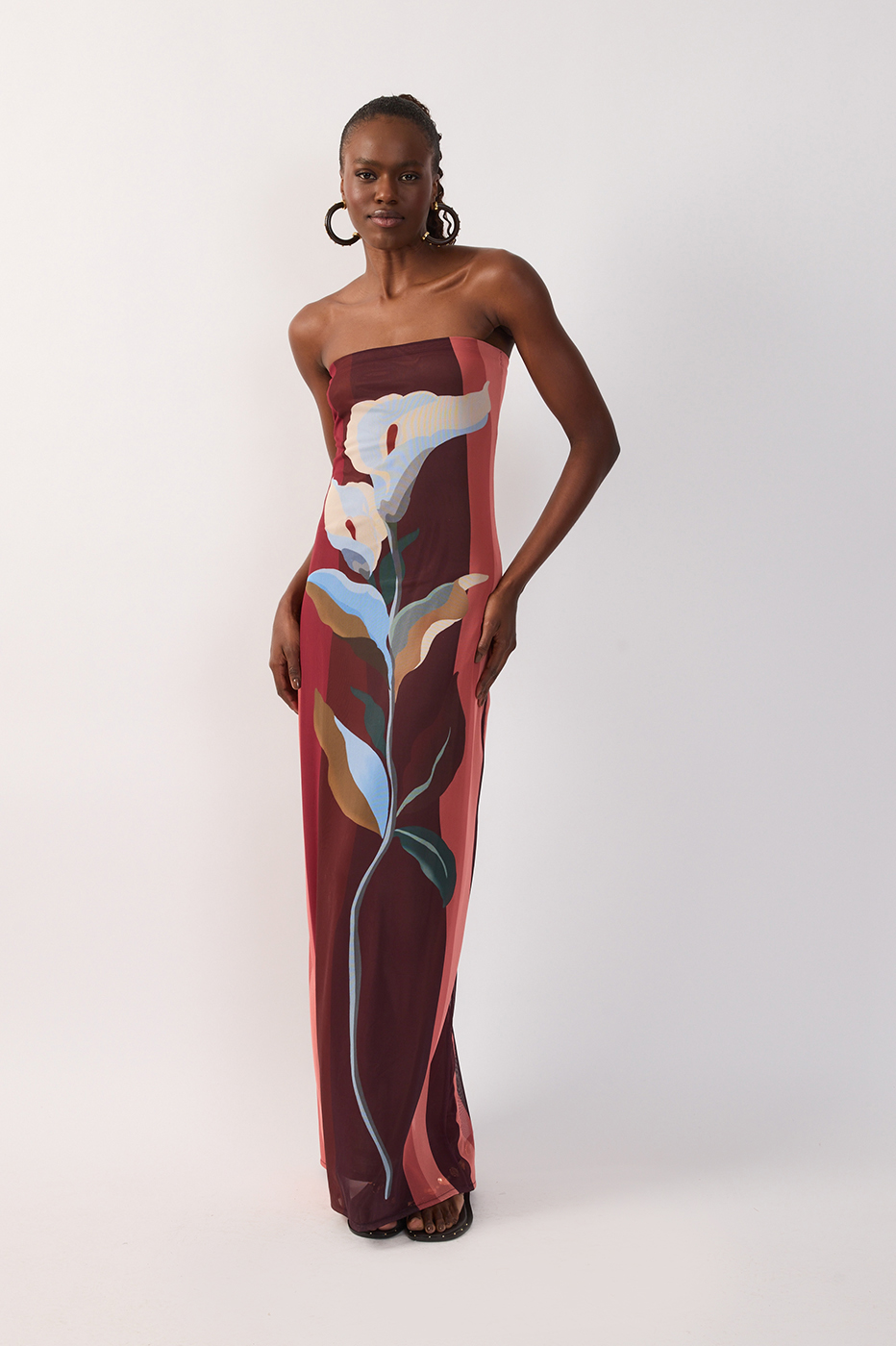A woman stands against a plain white background wearing the Dress To Multicolor B Risa Strapless Tulle Maxi—a floor-length tulle dress featuring a bold, botanical floral print in burgundy, blue, white, and pink—making it the ideal vacation evening dress for resort wear.