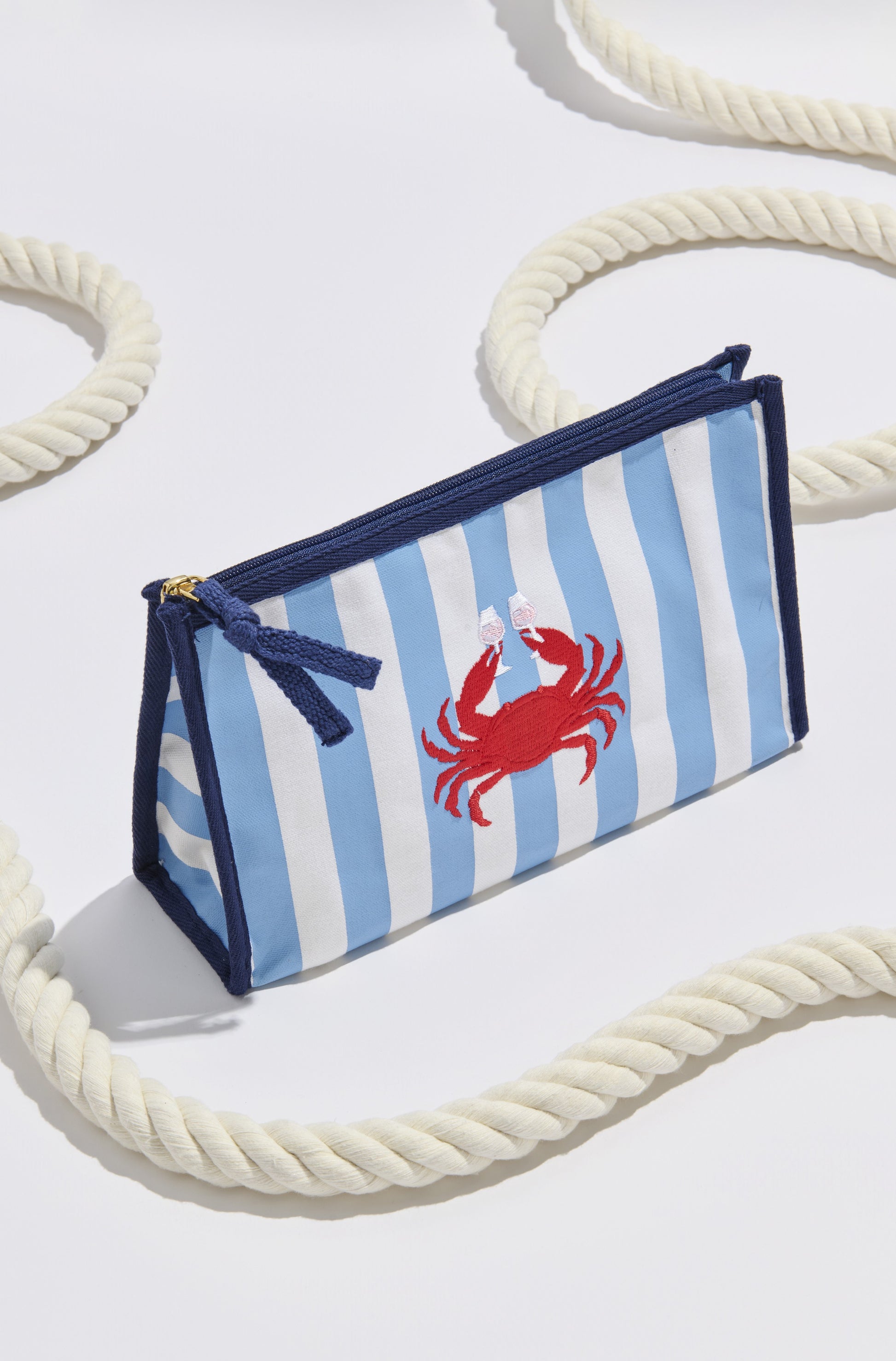 The Crab And Rose Zip Pouch by South Moon Under, in a Blue Multi color, rests on a white surface with coiled rope—ideal for carrying summer essentials.