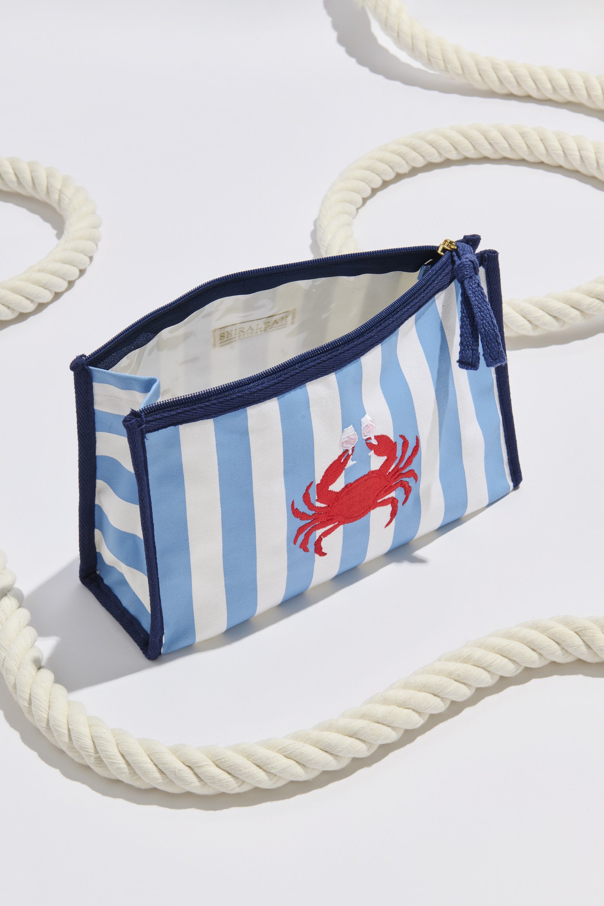 The Crab And Rose Zip Pouch by South Moon Under, featuring blue and white stripes with a red crab design, is shown on a white surface with thick rope—ideal for storing your summer essentials.