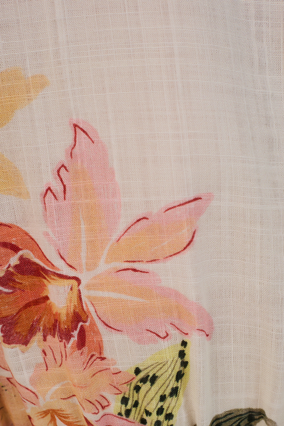 Close-up of the Flourish Tie Front Blouse by Dress To: a light, sheer fabric with a grid pattern, showcasing pastel pink, orange, and yellow florals with green leaves in a delicate botanical motif.