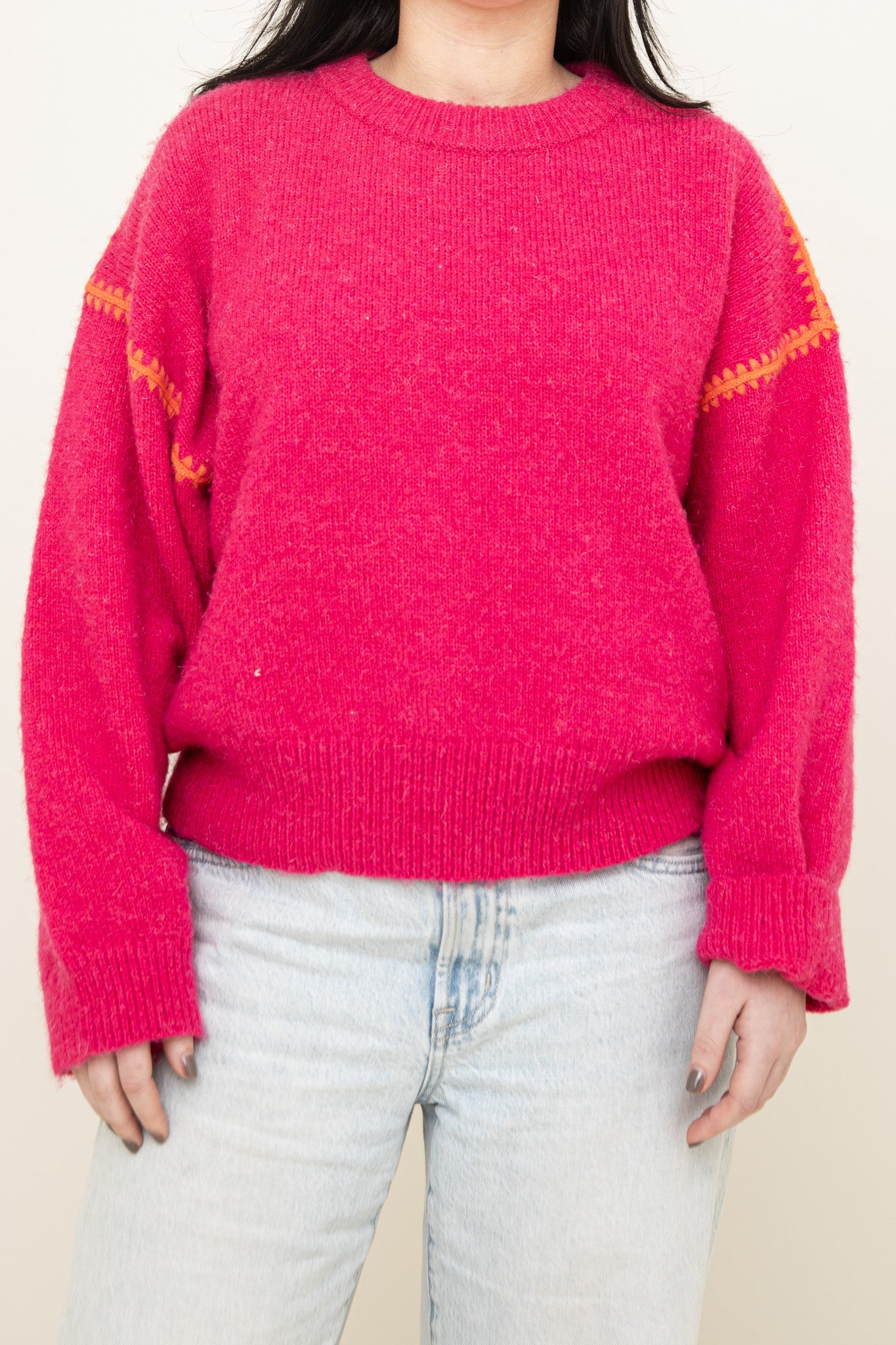 A person wearing The Jenny Sweater by Isla in hot pink with orange upper arm details and light-wash jeans, standing against a plain background.
