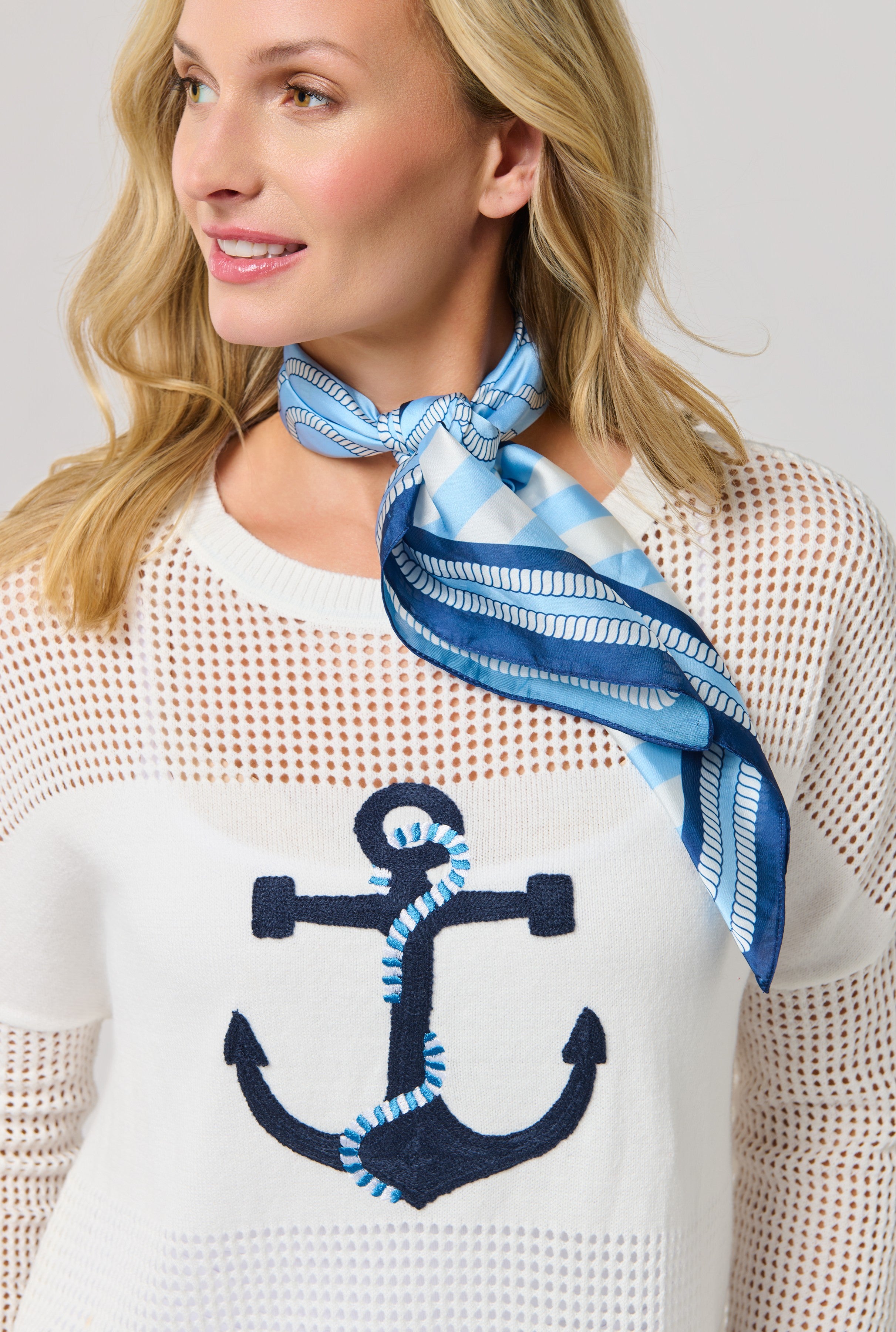 A woman smiles and looks to the side, wearing a white mesh sweater with a navy anchor design and the Coastal Scarf by South Moon Under tied sailor-chic around her neck.