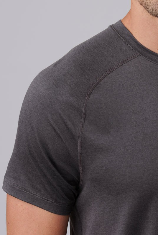 Close-up of a person wearing the South Moon Under Atmosphere Tee, a fitted short-sleeve dark gray shirt crafted from lightweight performance fabric, highlighting the upper chest, shoulder, neck, and arm against a plain light gray background.