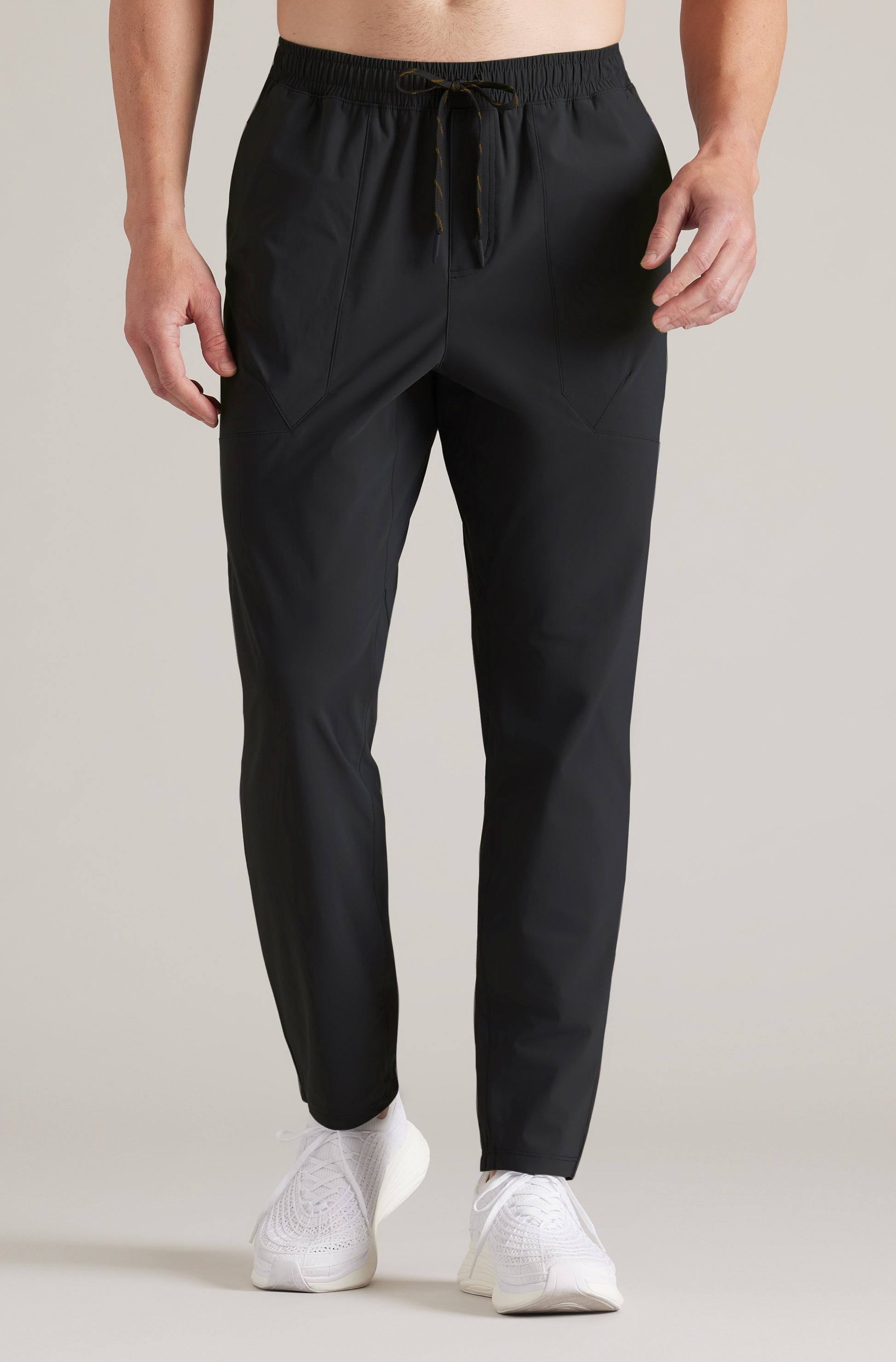 Someone wears the South Moon Under Pursuit Pant in BLACK, featuring an athletic jogger fit and drawstring waist, paired with white knit sneakers against a plain light background; upper body not shown.