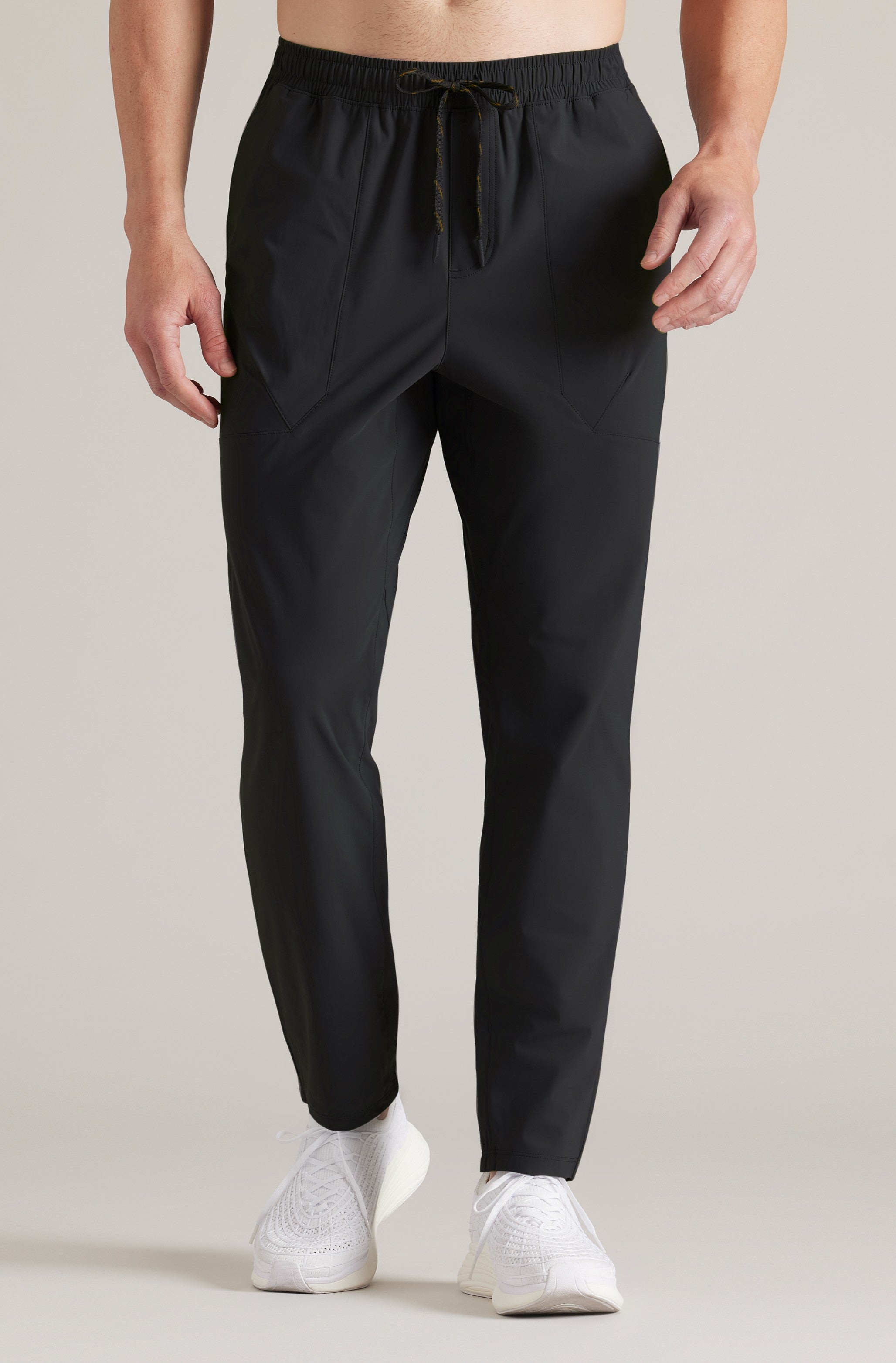 Someone wears the South Moon Under Pursuit Pant in BLACK, featuring an athletic jogger fit and drawstring waist, paired with white knit sneakers against a plain light background; upper body not shown.