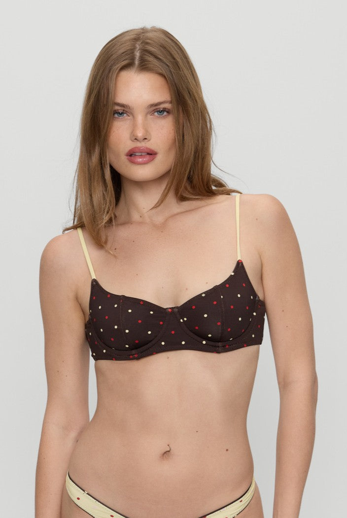 A woman with long, light brown hair wears the Frankies Bikinis Honey Bug Cola Satin Top. She poses against a plain light gray background.