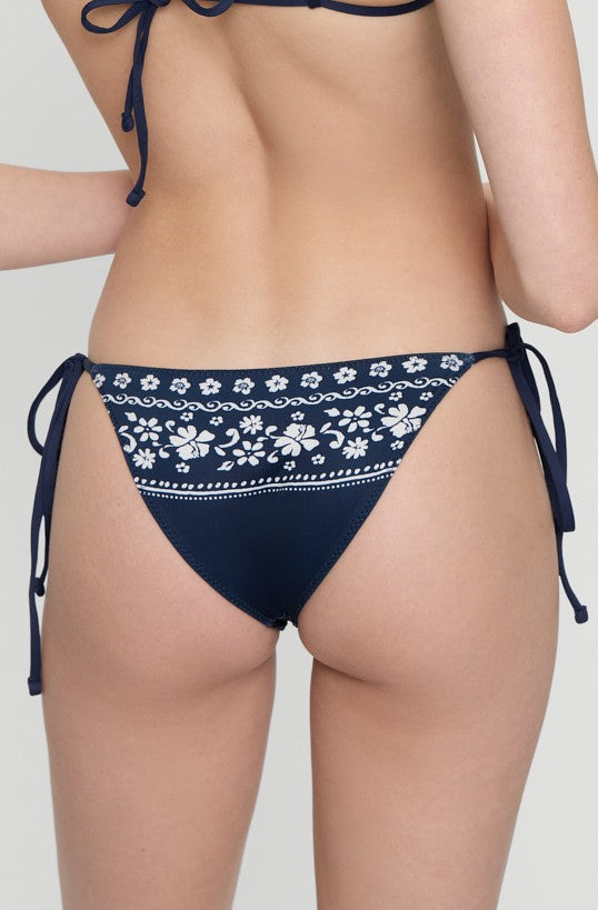 A woman is shown from the back wearing the Frankies Bikinis Malibu Blue Mackenzie Bottom, featuring a navy floral pattern and side ties against a light background—ideal for vacations or as a timeless swimwear staple.