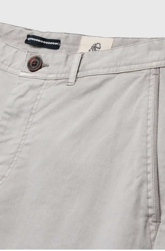 Close-up of the Andrew Stretch Twill Short by Surfside Supply Co. in light gray, highlighting the cotton spandex waistband, brown button closure, belt loop, side pocket, and a white label with a black lion illustration inside the waistband.