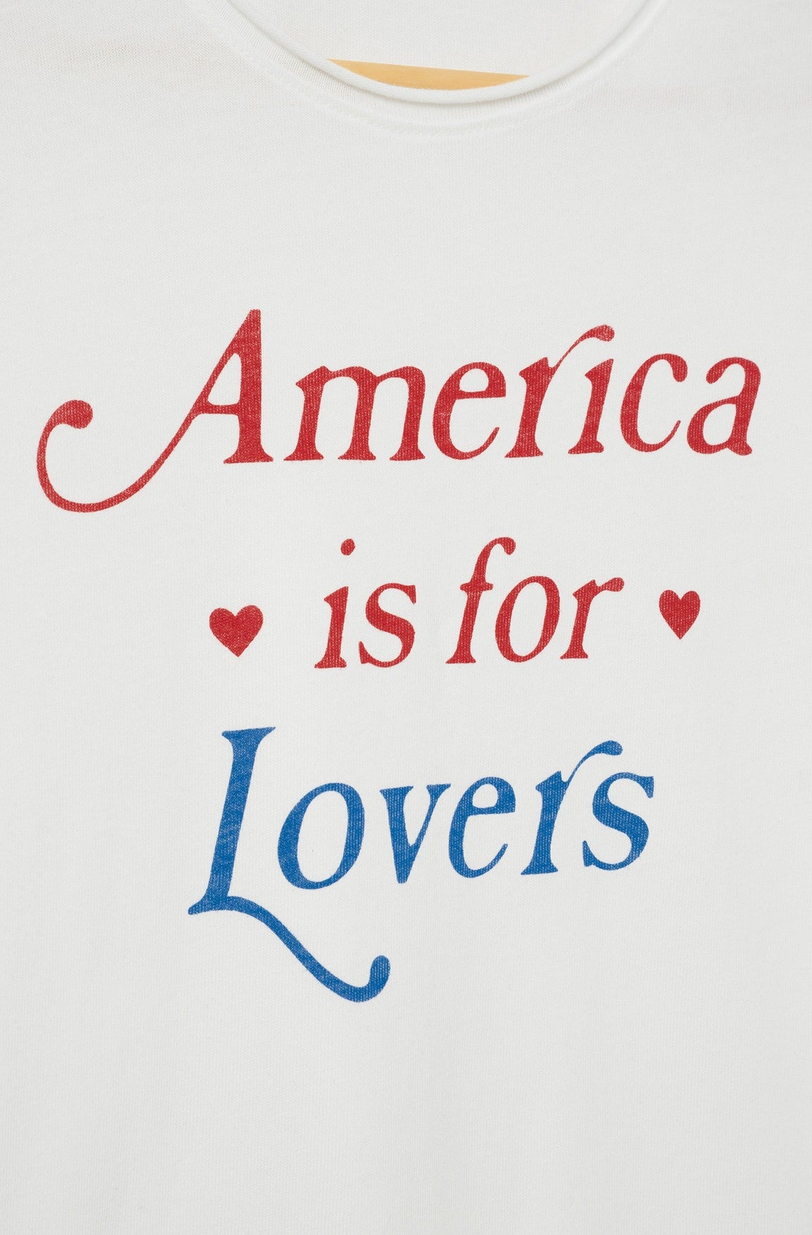 White crew neck shirt by Original Retro Brand, featuring red "America is for" text with blue "Lovers" below and small red hearts flanking "is for." Product name: America Is For Lovers. Color: White. Relaxed fit.