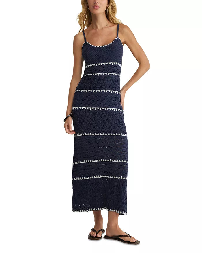 A woman stands with one hand on her hip, wearing the Z Supply Catamaran Striped Maxi Dress in Navy Multi, paired with black flip-flops and a black bracelet.