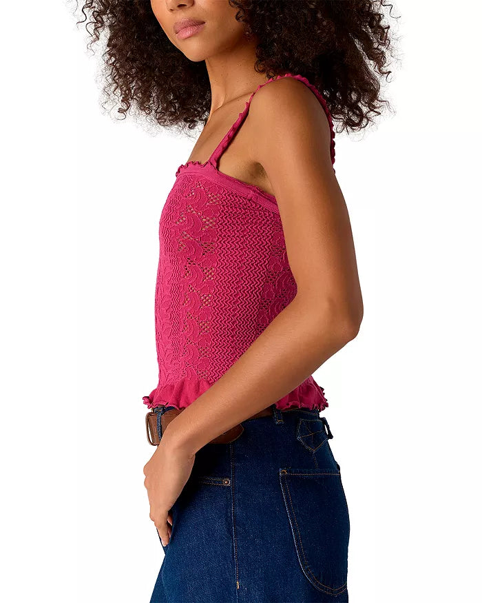 Woman with curly hair wearing the Free People So Soft Femme Square Top, a sleeveless textured pink top, and dark blue jeans, shown from the side with her hand resting on her hip.