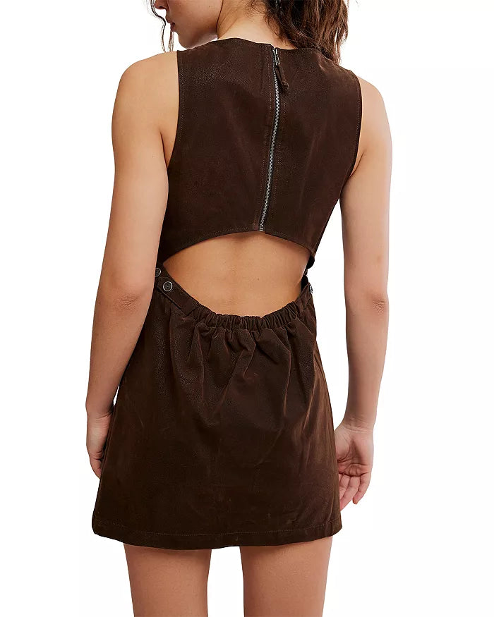 A woman is shown from behind against a white background wearing the Free People Atlas Suede Mini Dress—a sleeveless, dark brown A-line dress with an open back, a zipper closure, and a gathered elastic waist detail.