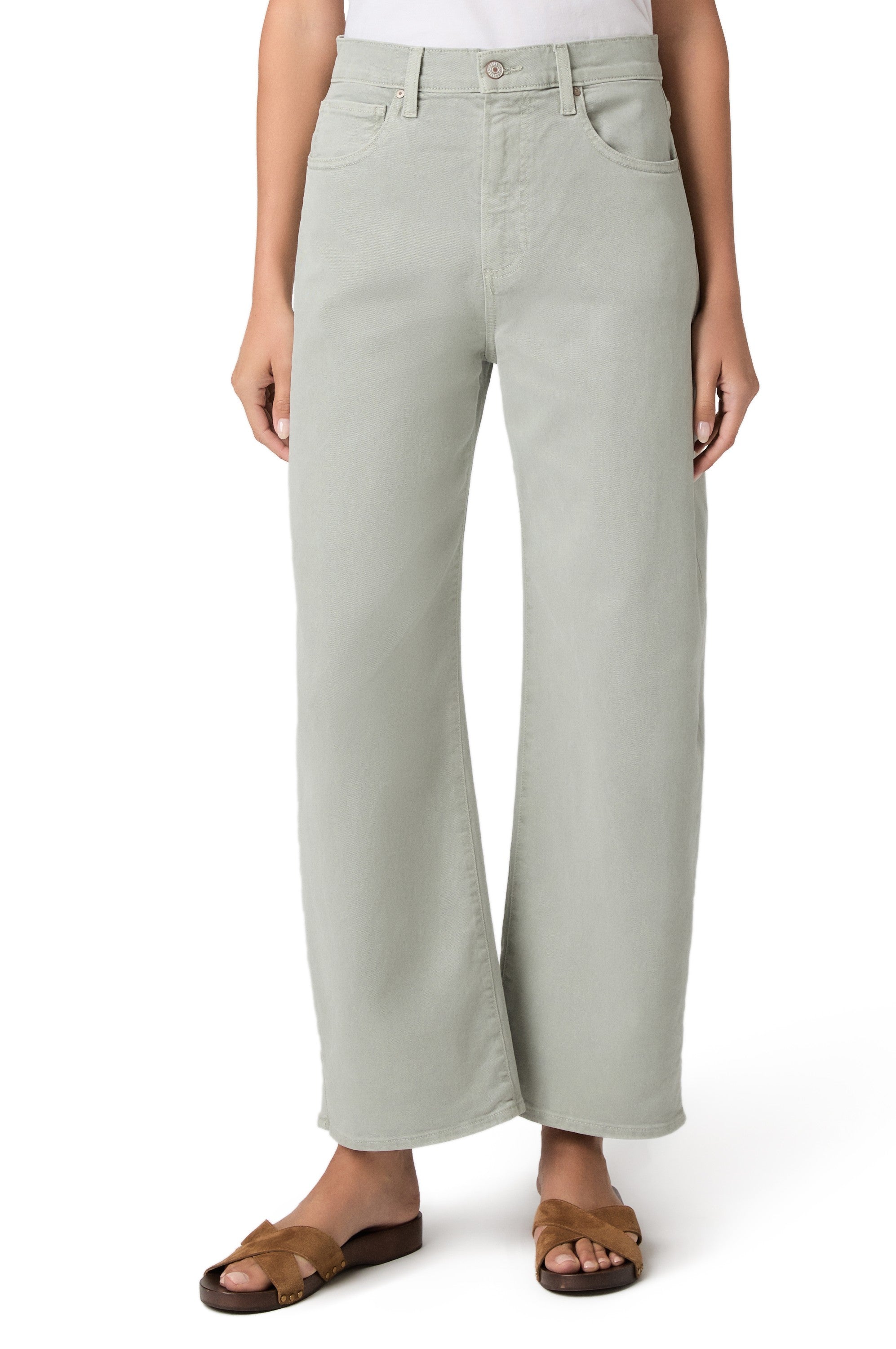 A person wearing the Paige Ariella In Sea Glass high rise barrel leg jeans in light green, a white top, and brown sandals stands against a plain white background.