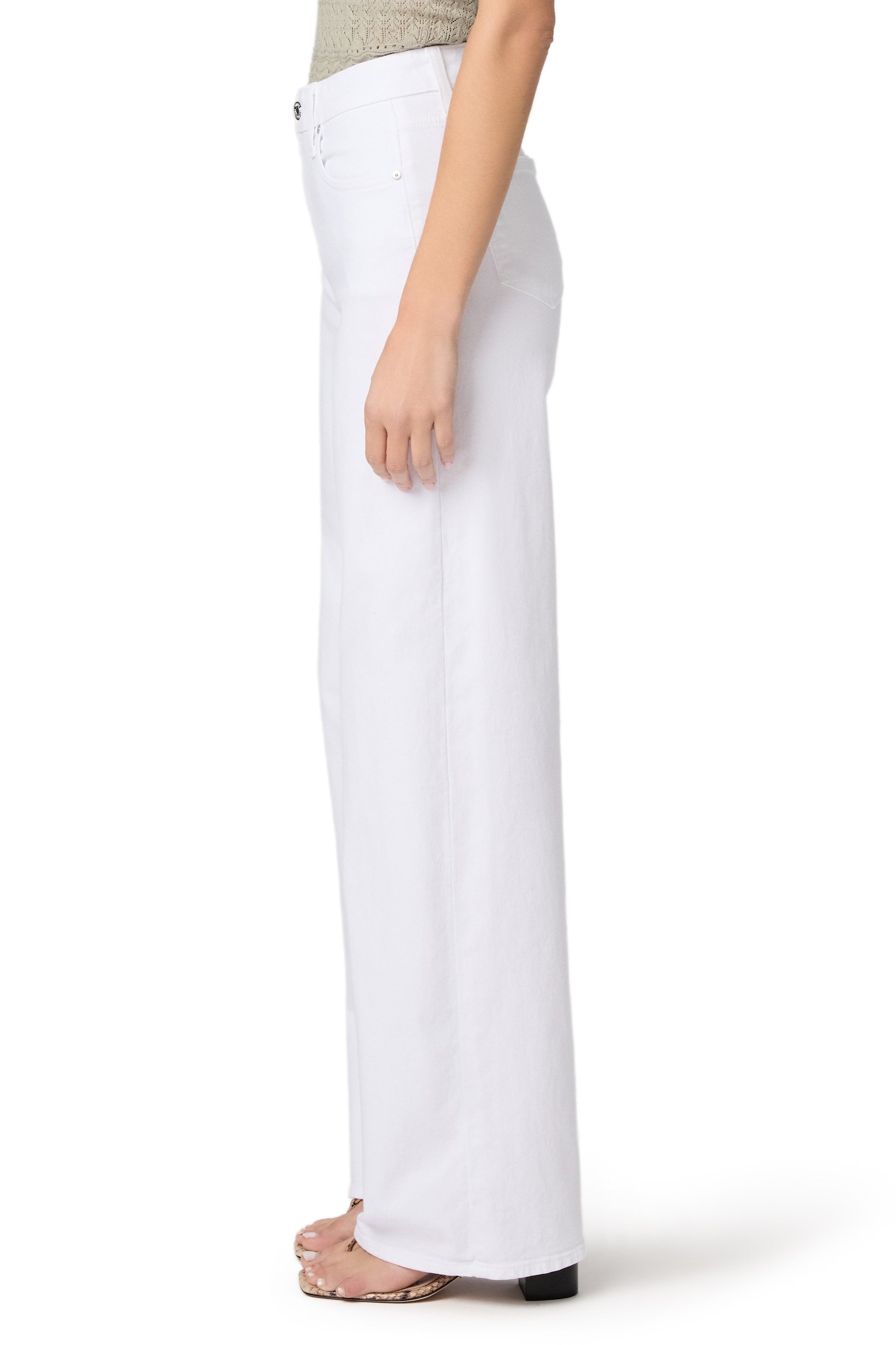 A person is shown from the waist down wearing Paige’s Tatum 32 In Crisp White relaxed fit, high-waisted jeans with open-toed sandals, set against a plain white background.