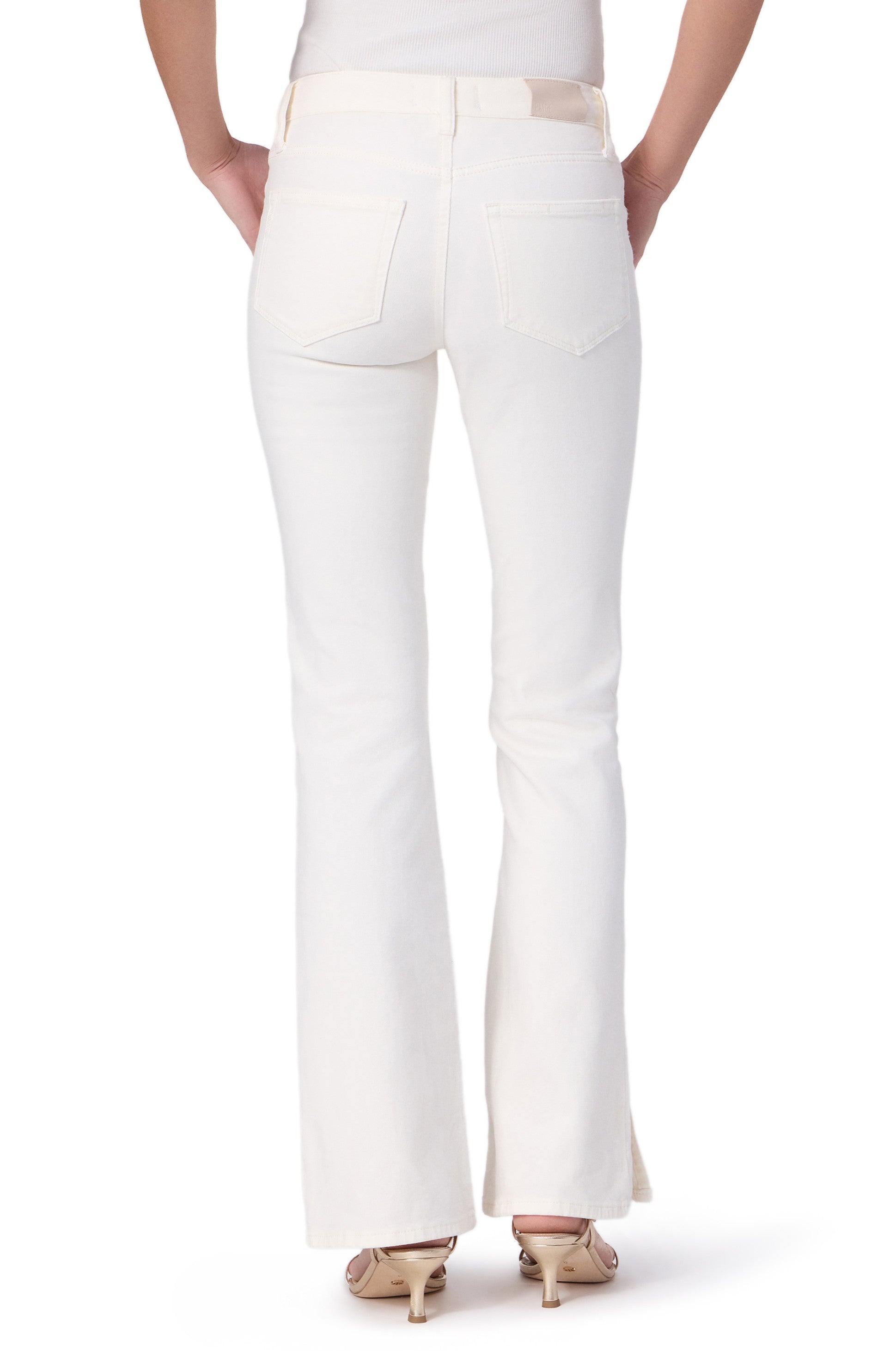 A person is shown from the back against a white background, wearing Paige Laurel Canyon 32" with Forward Panel + Vent stretch denim bootcut jeans and beige heeled sandals, hands on hips to highlight the flattering silhouette.