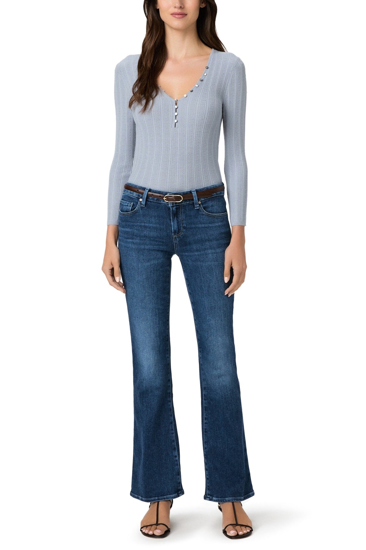 Woman wearing light blue ribbed long-sleeve henley top and dark blue low-rise bootcut jeans with brown belt.