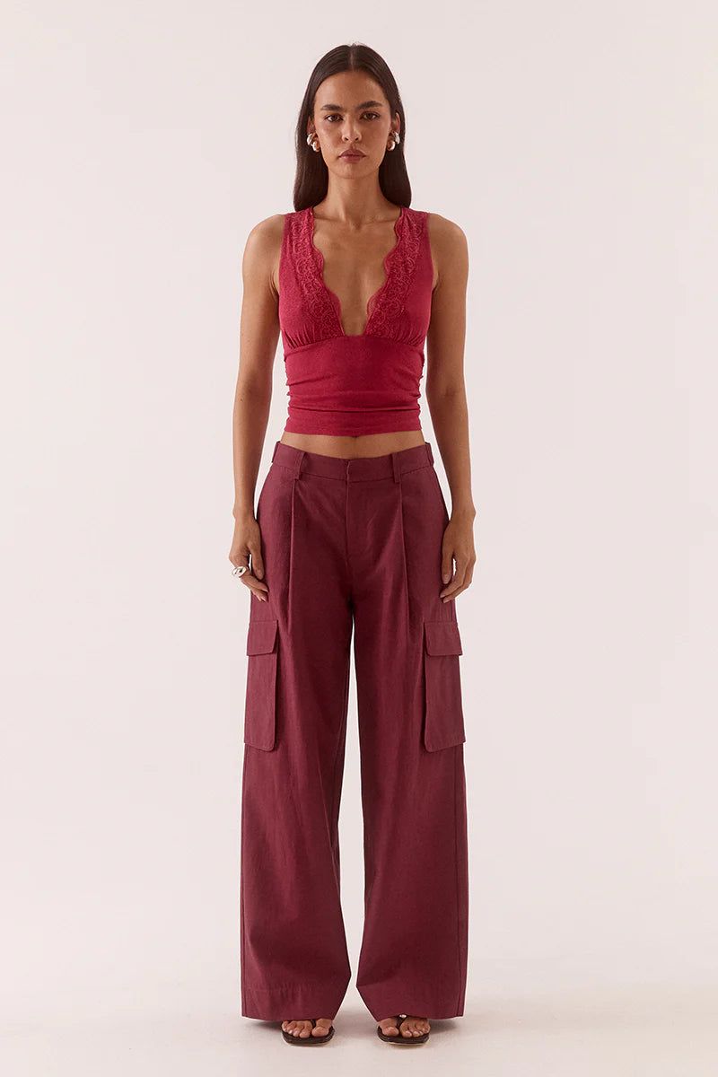 A woman faces forward in the red "Loni Top" by Sovere—fitted with textured stretch mesh and a deep V lace trim neckline—styled with matching high-waisted wide-leg cargo pants and black sandals, set against a plain light background.