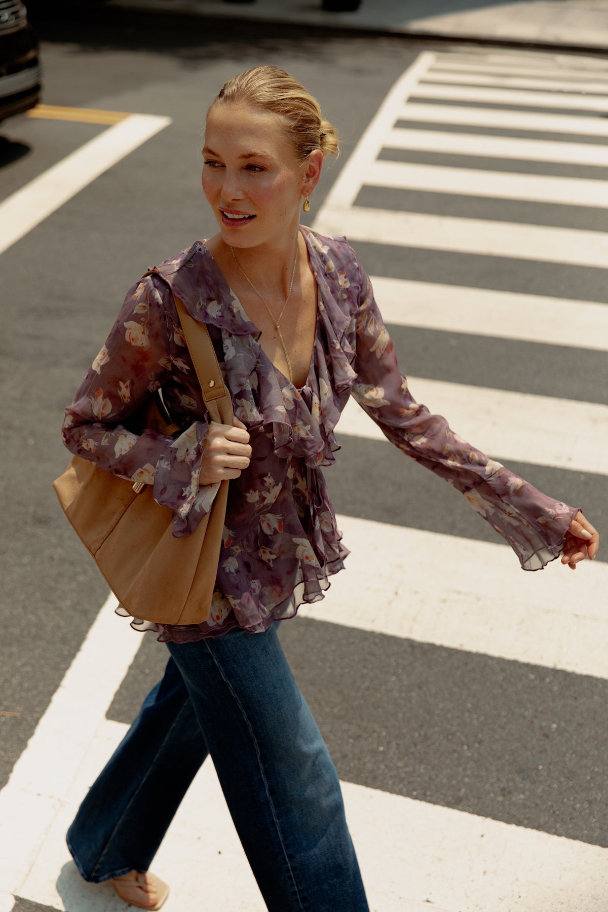 Mauve floral print blouse with ruffled edges and long sleeves, worn with blue jeans and tan shoulder bag.