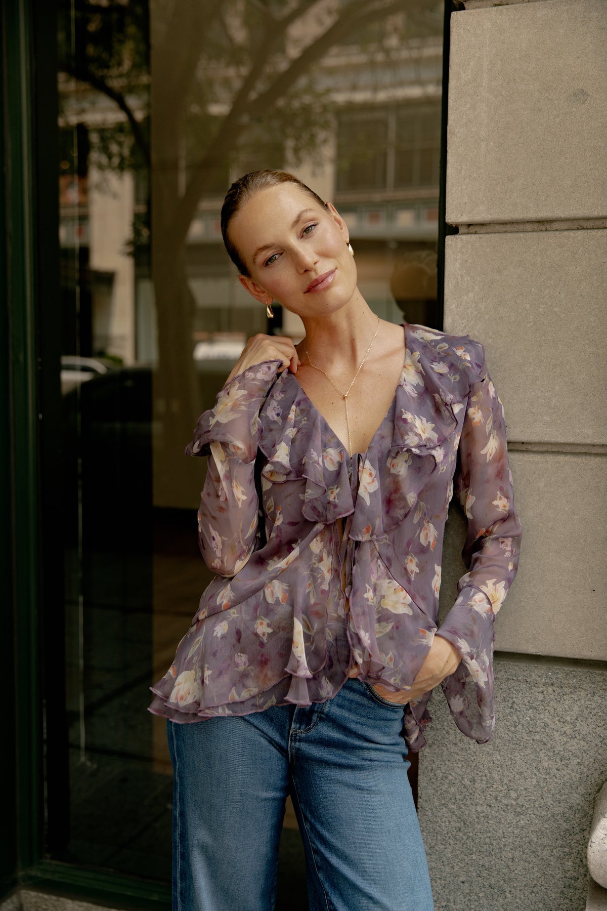 Purple floral blouse with ruffled front and long sleeves, worn with blue jeans.