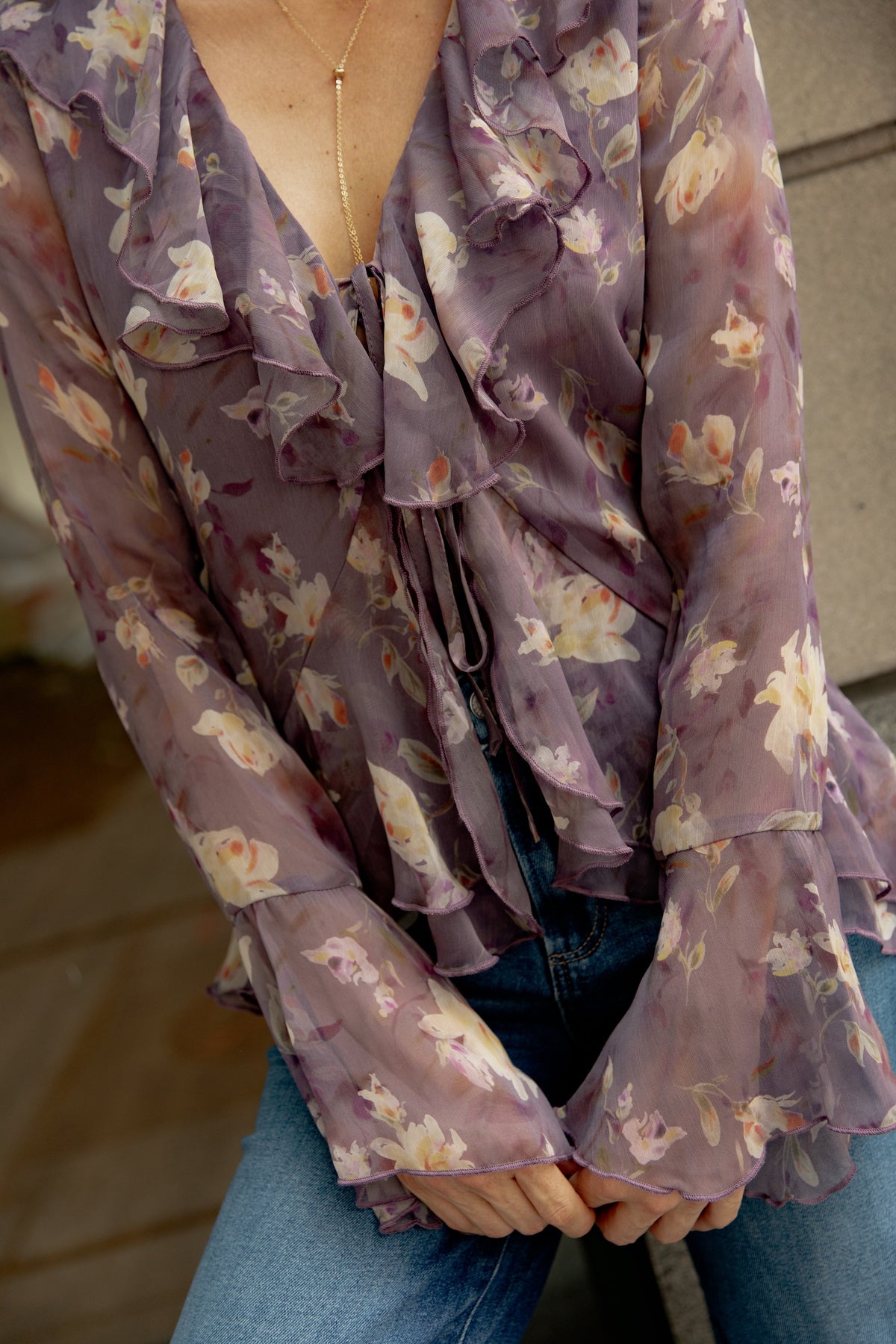 Mauve floral blouse with ruffled front placket and long sleeves, styled with blue jeans.