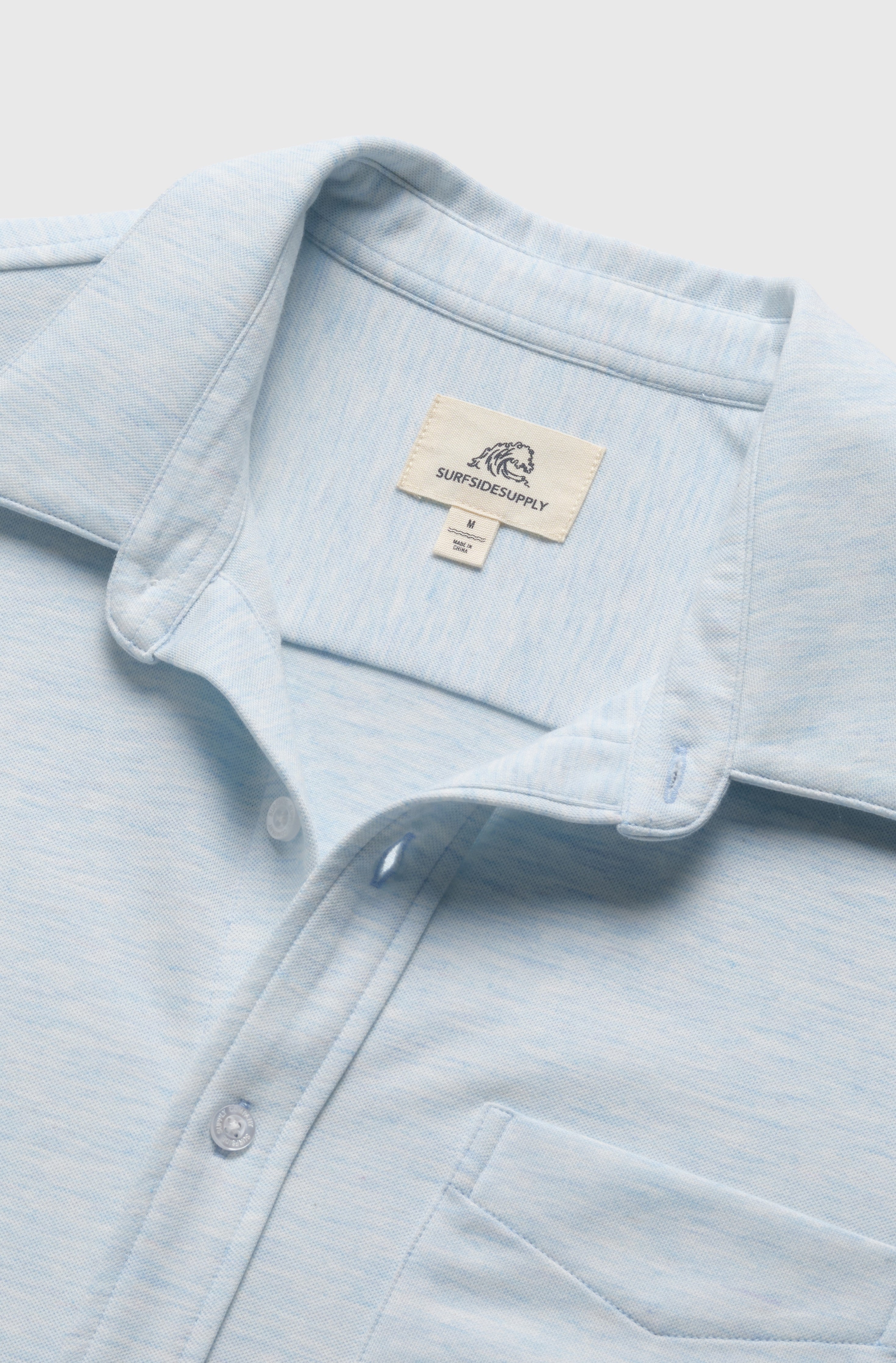 The Tony Short Sleeve Burnout Knit Shirt by Surfside Supply Co. features a light blue regular fit, white buttons, chest pocket, and visible inner collar label. The button-front shirt is neatly laid flat on a white background.