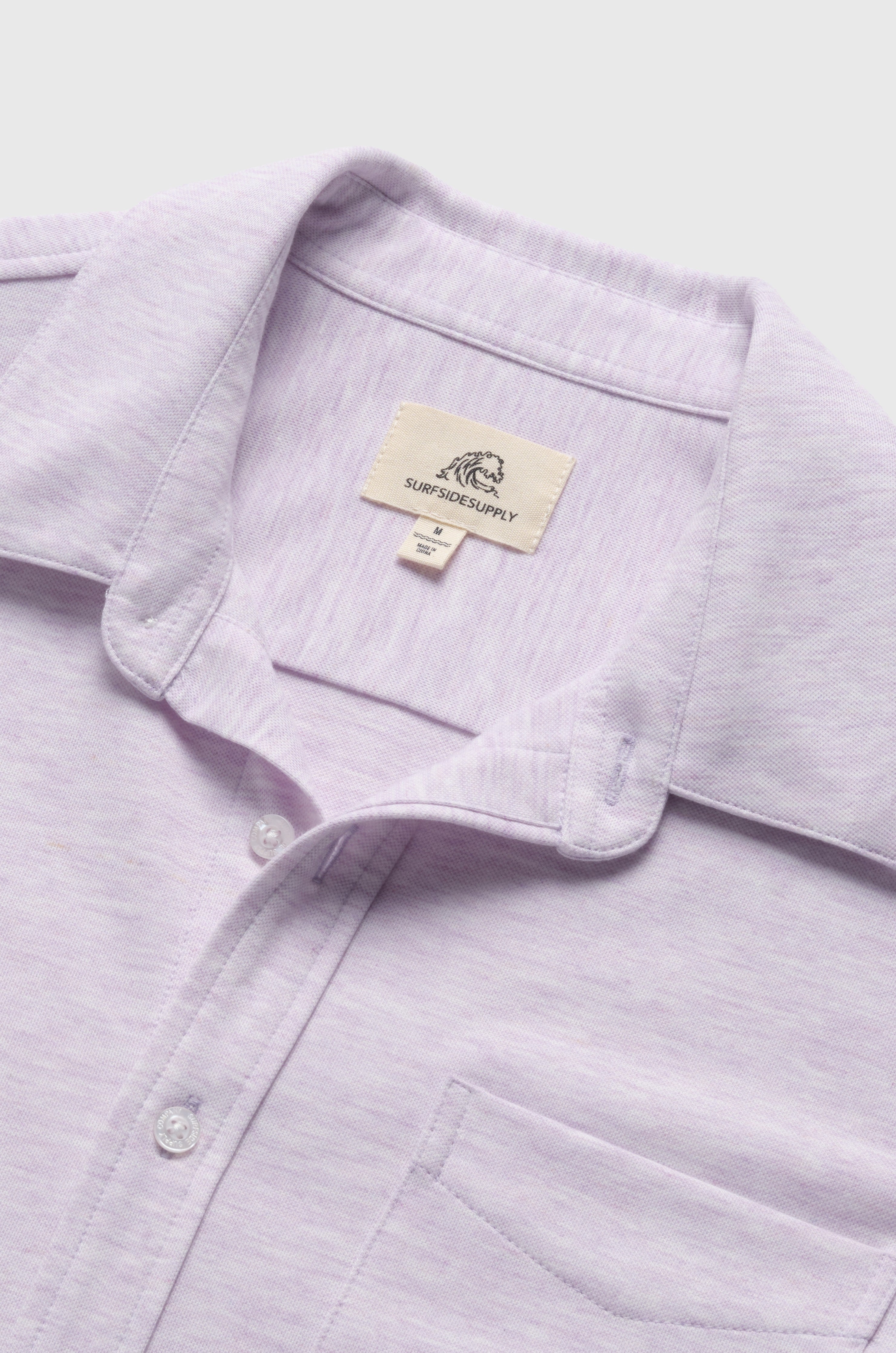 A close-up of the Tony Short Sleeve Burnout Knit Shirt in light purple by Surfside Supply Co., featuring white buttons, a front pocket, and a brand label inside the collar.