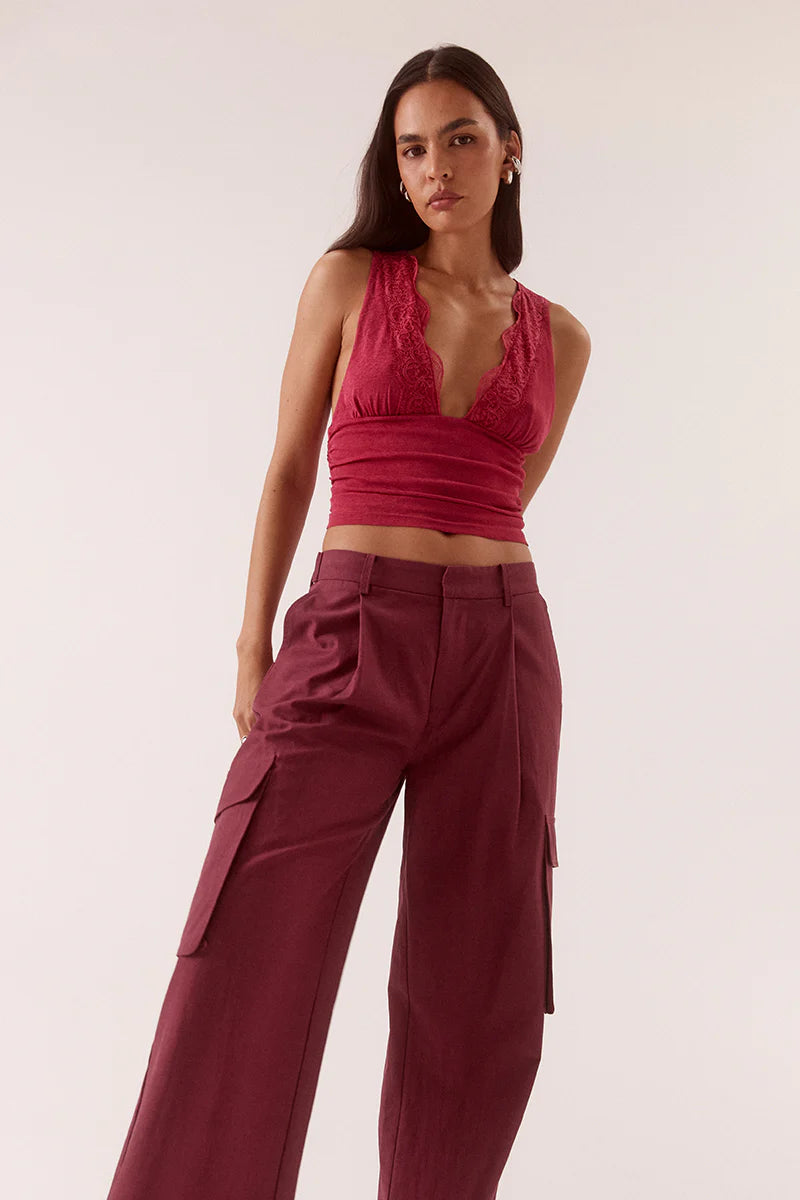 A woman wears the Sovere Loni Top, a sleeveless lace V-neck, paired with high-waisted wide-leg maroon cargo pants against a light, neutral background.