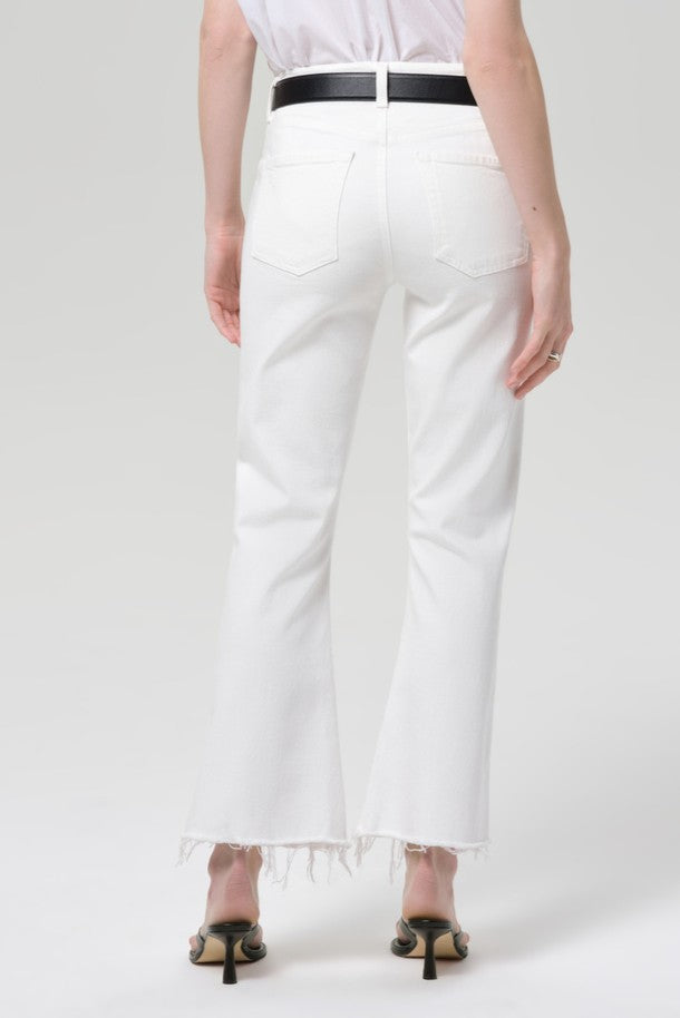 A person stands facing away against a light background, wearing Citizens of Humanity Goldie Kick Flare 27 Raw Hem jeans, paired with a black belt and black heeled sandals.