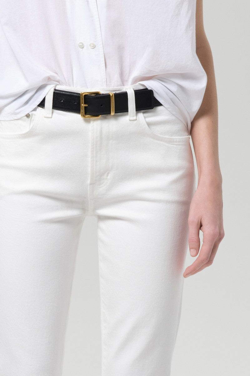 A person wears a white button-up shirt tucked into Citizens of Humanity’s Goldie Kick Flare 27 Raw Hem jeans; only the torso and upper legs are visible.