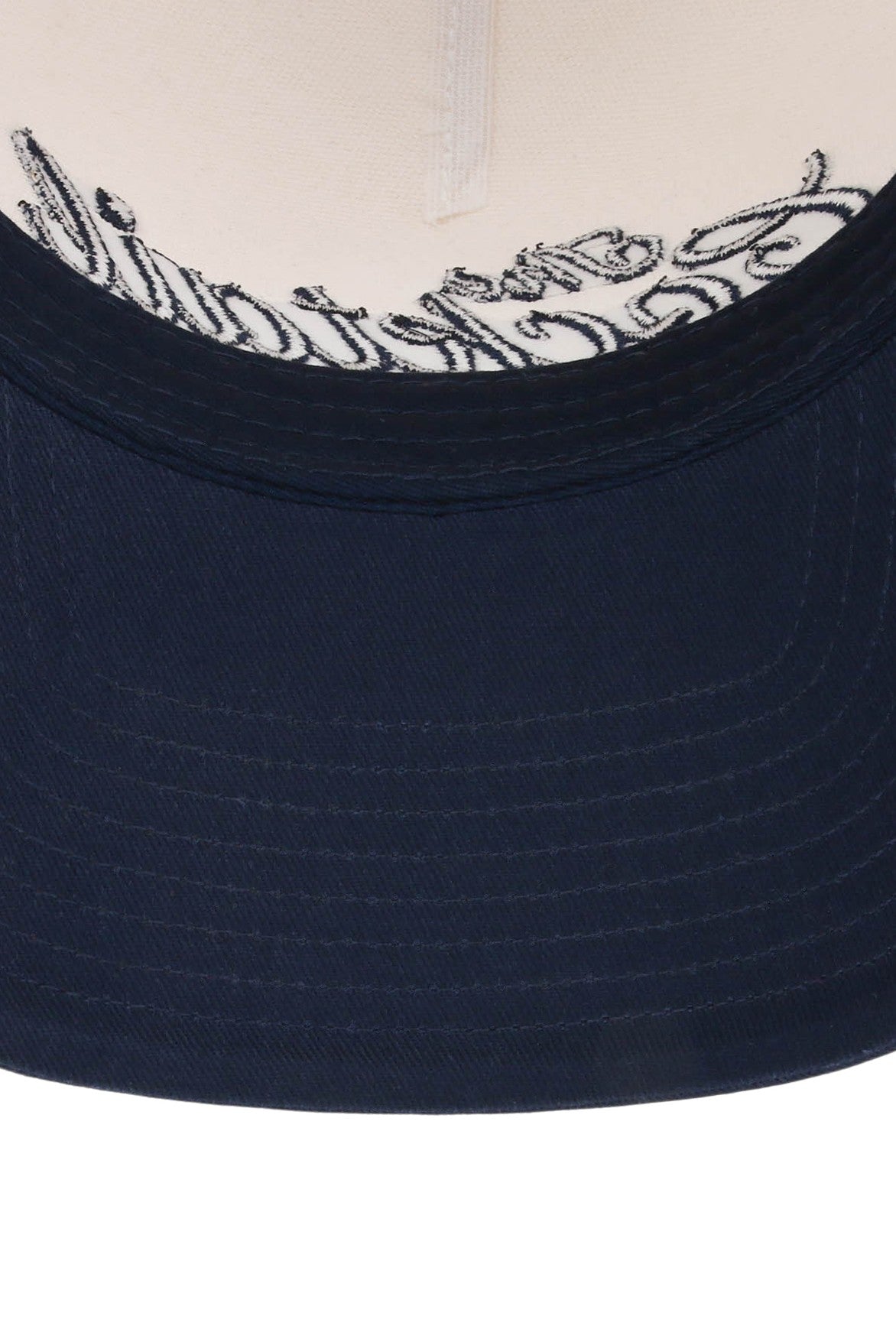 The underside of the Smu Cocktail Club 5-panel Hat’s navy blue brim by South Moon Under, revealing white fabric above and partially visible black cursive writing on the inside.