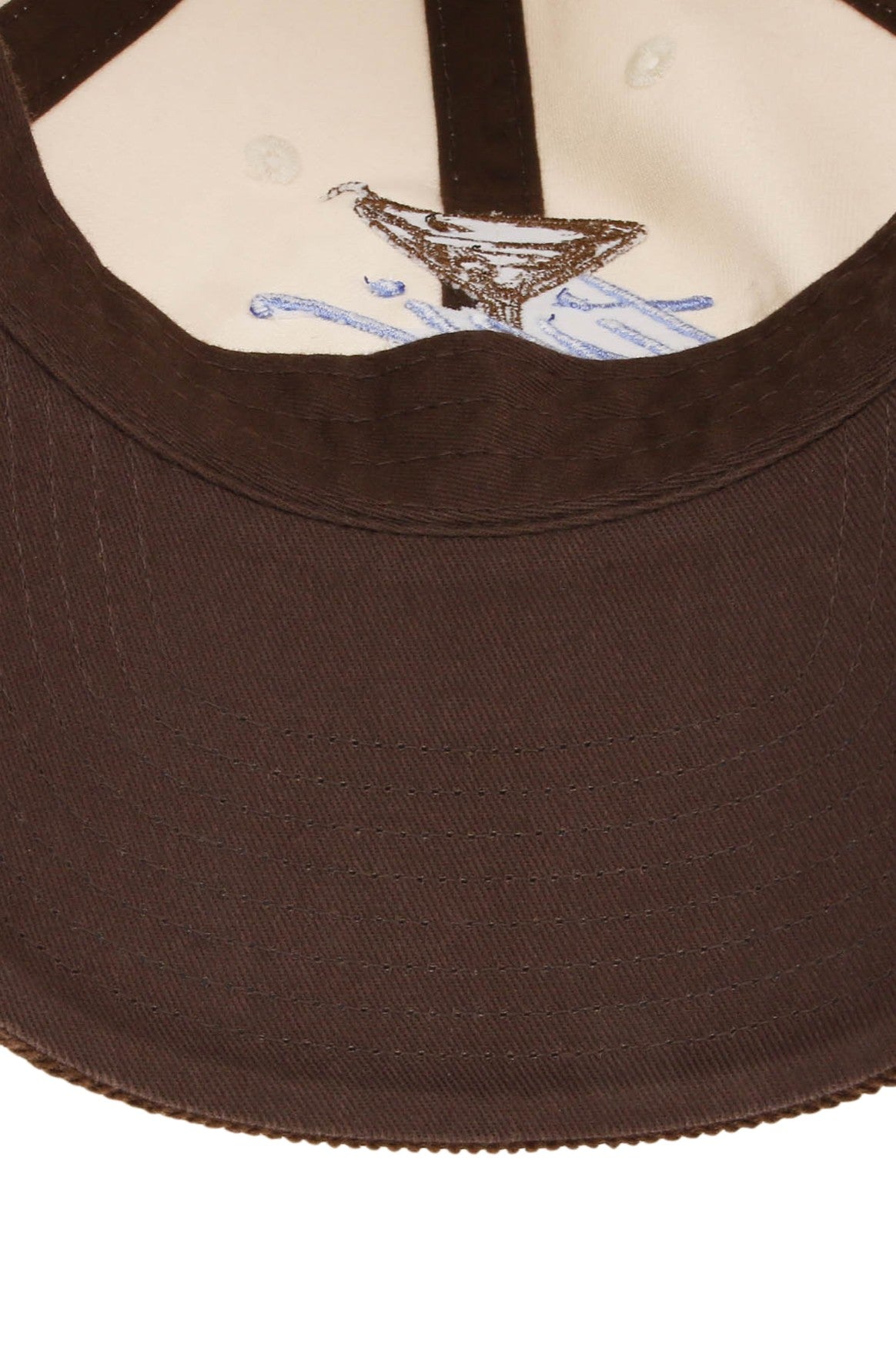 Close-up of the underside of the South Moon Under Smu Tini Time Cap, a brown snapback baseball cap, revealing the white inner fabric and a small embroidered martini glass with partially visible blue text on the lining.
