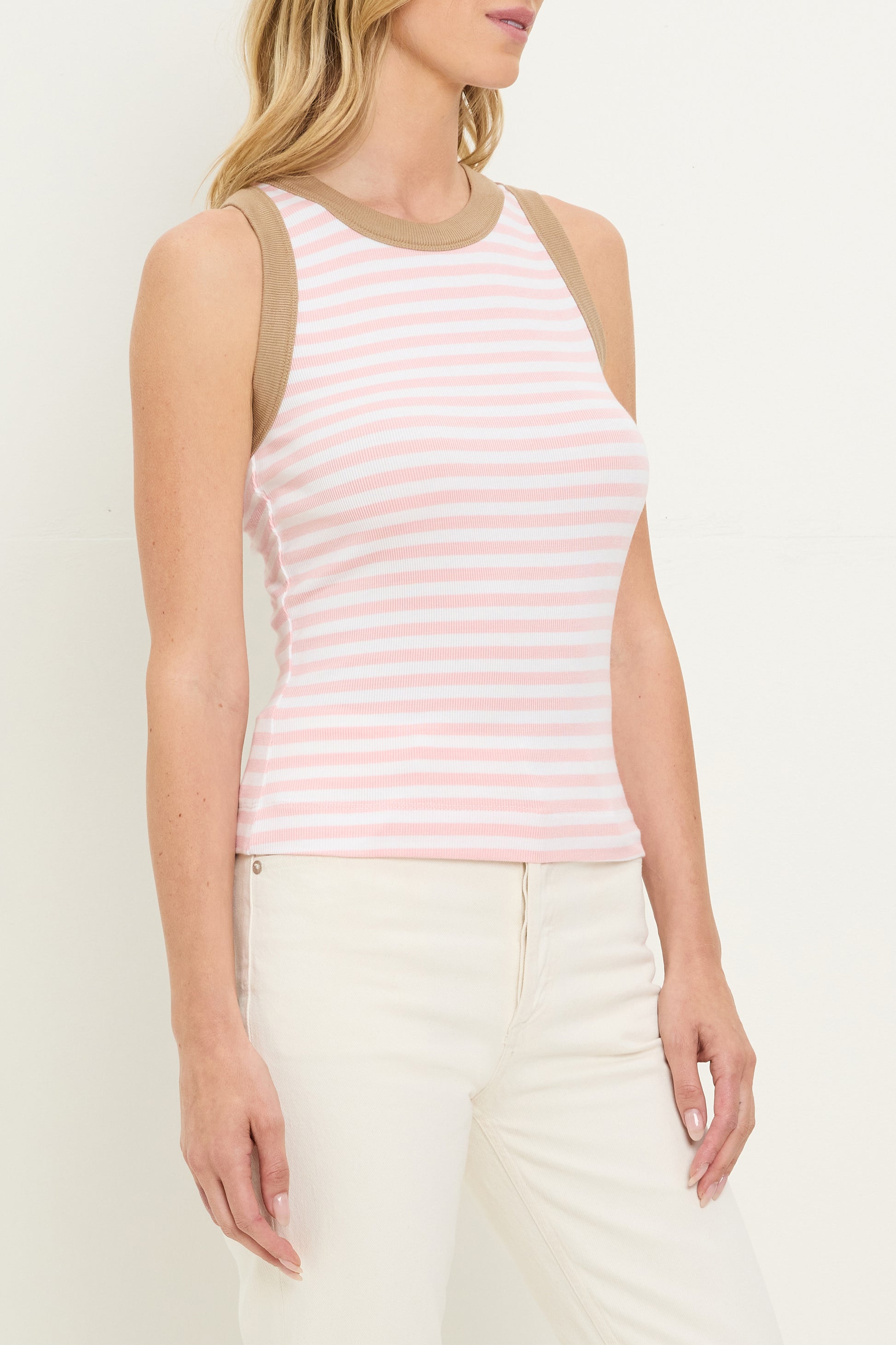 A woman wears the Michael Stars Gina Ringer Tank, a fitted pink and white striped top made from Ultra Rib fabric, styled with cream pants.