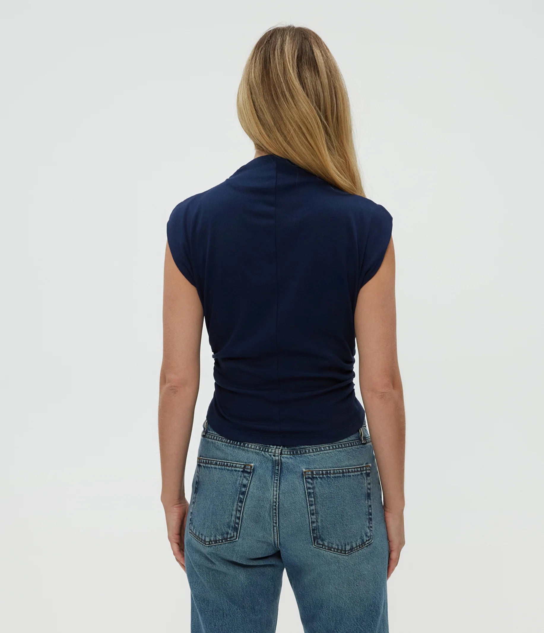 A person with long, straight blonde hair is shown from the back wearing the Michael Stars Amara Crop Top in Nocturnal and medium-wash blue jeans, set against a plain white background.