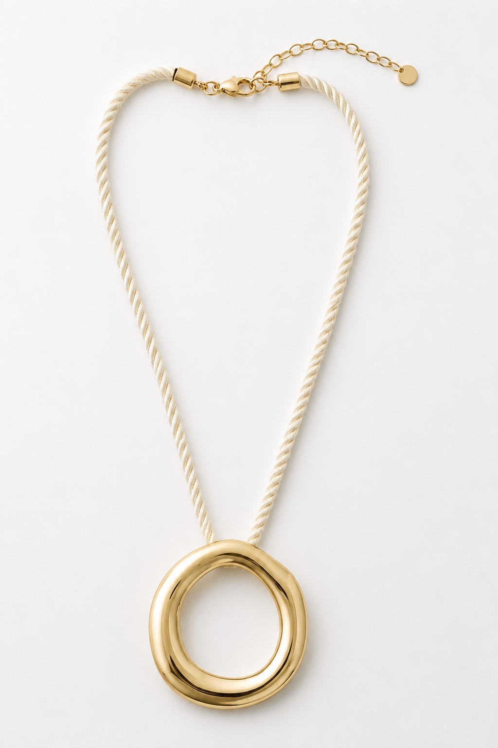 The Ettika Open Circle Corded Pendant features a gold organic-shaped pendant on a thick cream cord with a gold clasp and extender chain, shown against a plain white background.