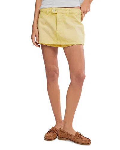 A person wearing the Galivanting Skort by Free People in light yellow with dart seaming, paired with a white top and brown moccasin-style shoes, stands against a plain white background.
