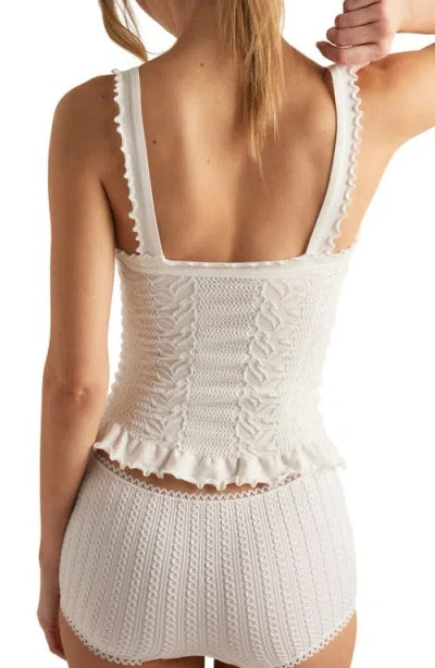 A person stands with their back to the camera, wearing the Free People So Soft Femme Square Top—a white knitted tank top paired with high-waisted shorts featuring textured patterns and scalloped edges.