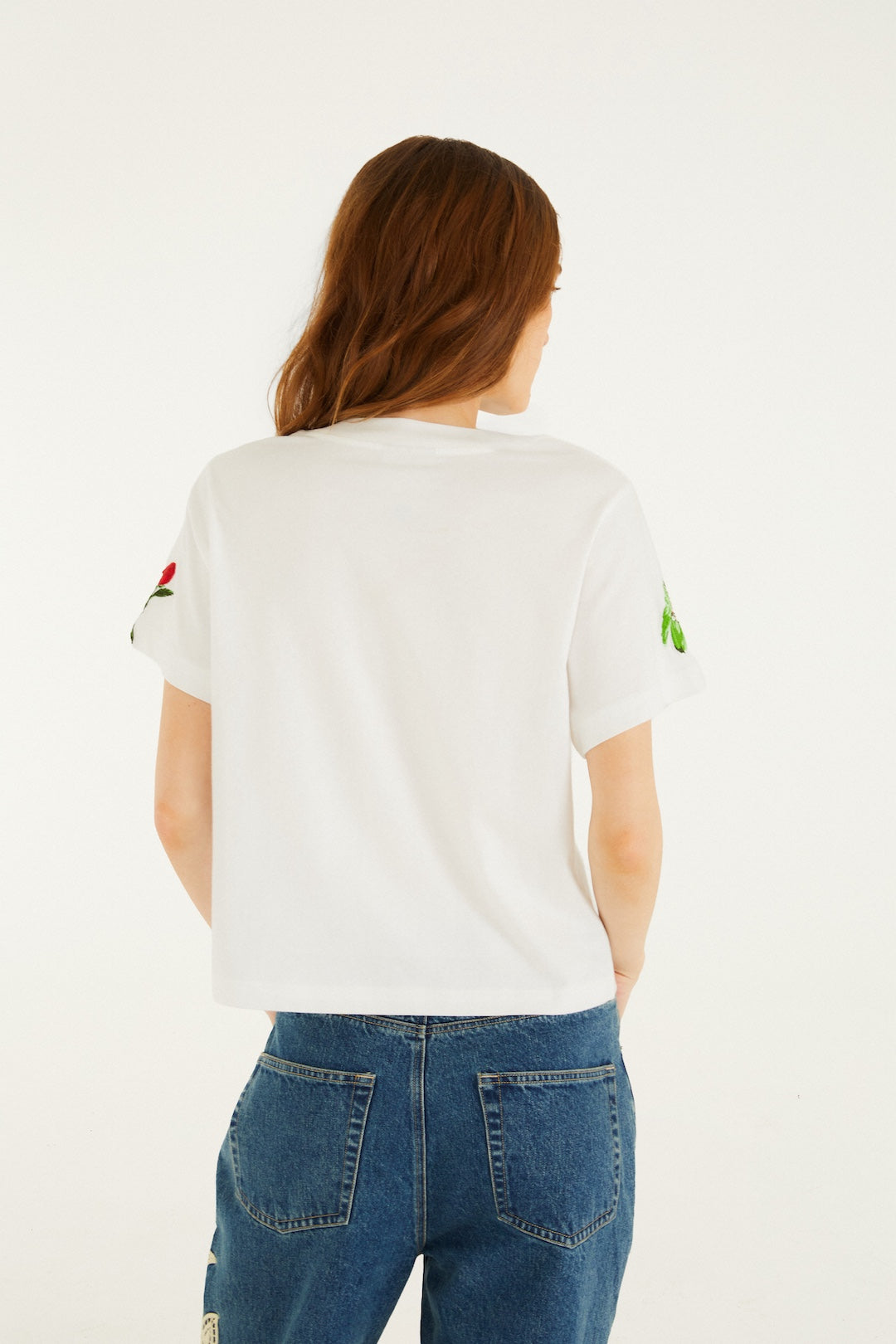 A person with long brown hair, wearing the Farm Rio Cool Day Relaxed T-shirt in off-white and blue jeans, stands facing away from the camera against a light background.