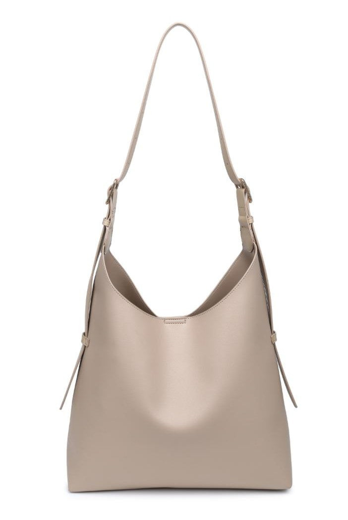 The Maria Tote by Urban Expressions is a beige faux leather shoulder bag with a minimalist design, adjustable strap, and subtle side buckle details, shown against a white background.