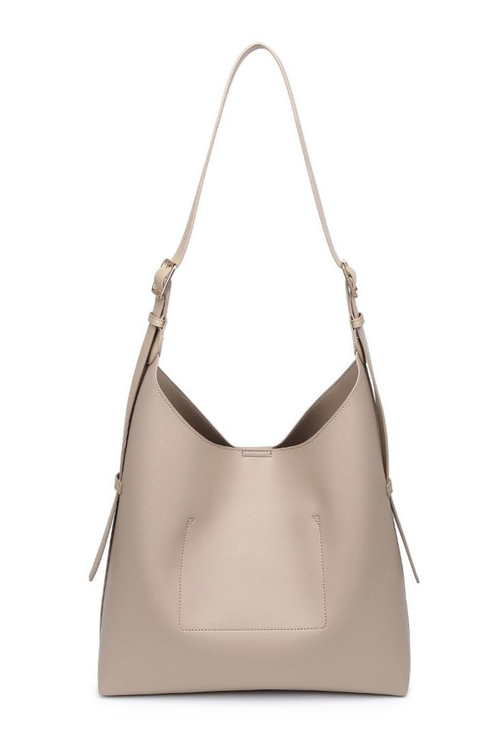 The Urban Expressions Maria Tote is a beige faux leather shoulder bag with an adjustable strap, front patch pocket, and minimalist design. It features a slightly curved top and is shown against a white background.