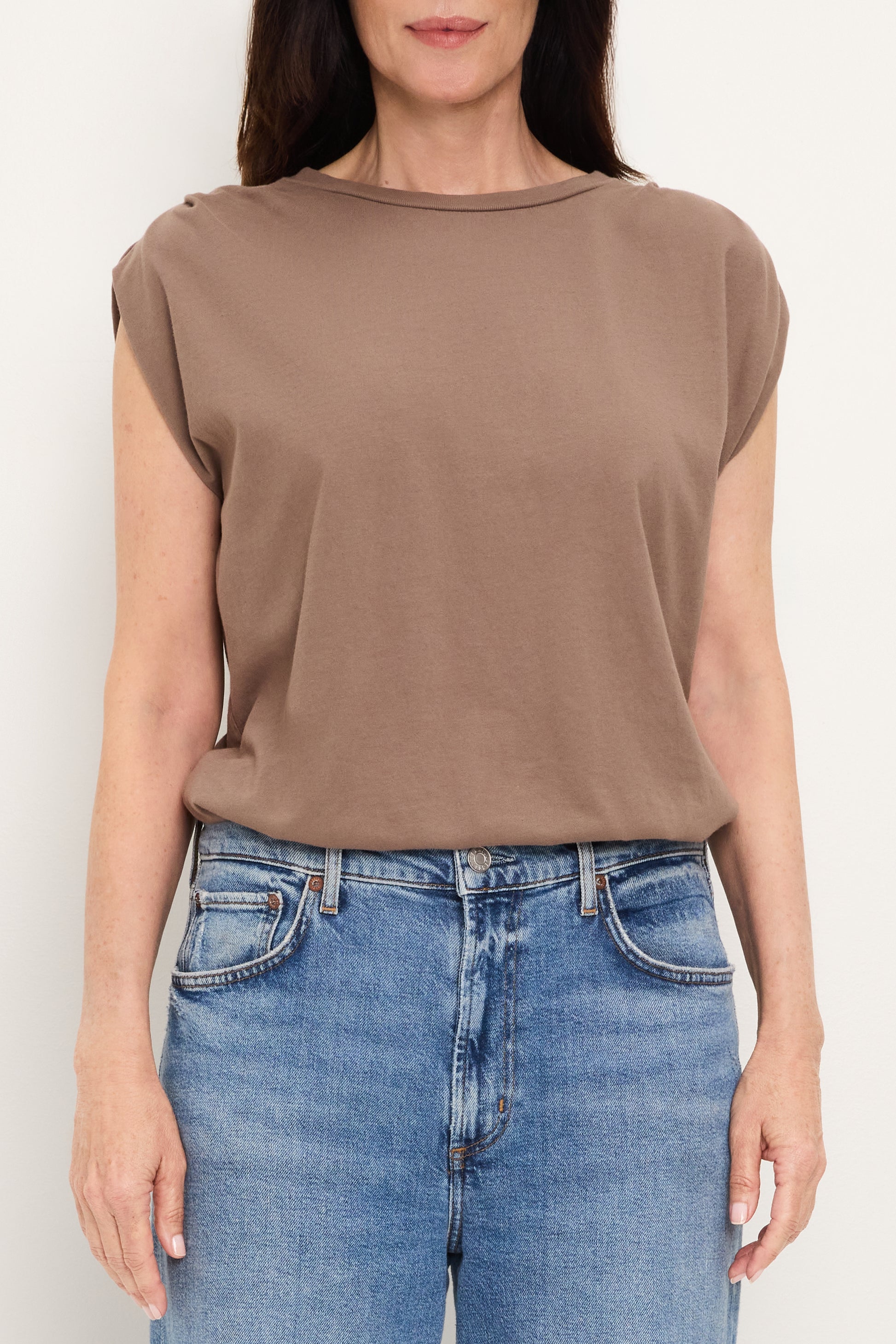 A person wears the Michael Stars Luca Bubble Tee in Quicksand—a relaxed-fit, sleeveless top—paired with blue jeans, standing against a plain white background with arms by their sides.
