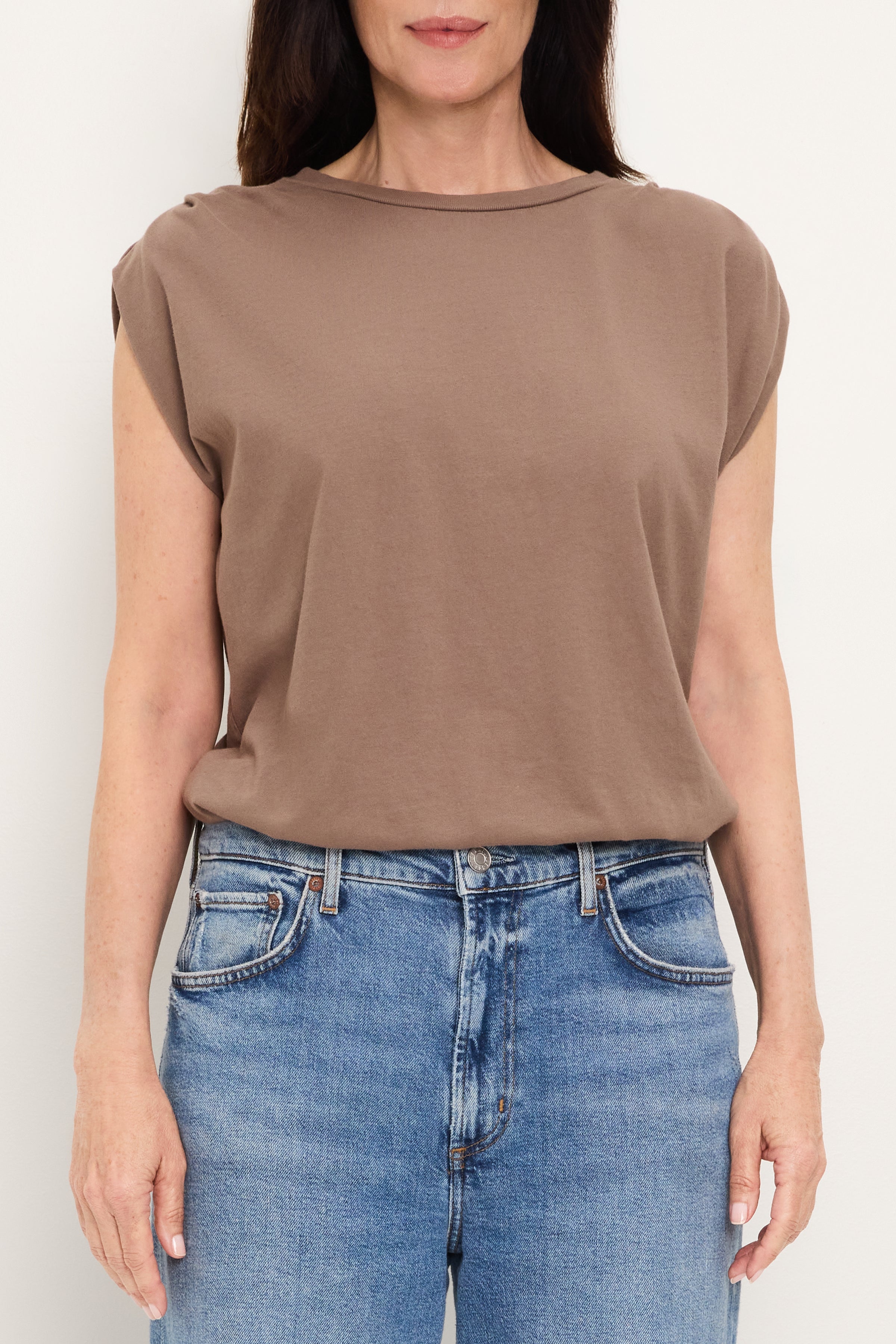 A person wears the Michael Stars Luca Bubble Tee in Quicksand—a relaxed-fit, sleeveless top—paired with blue jeans, standing against a plain white background with arms by their sides.