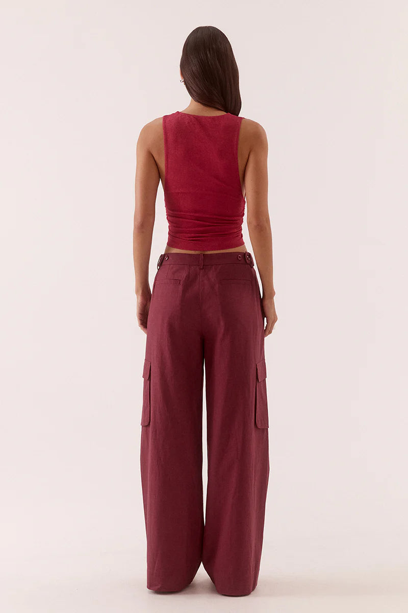 A woman with straight hair stands facing away in a maroon Sovere Loni Top paired with high-waisted, wide-leg maroon cargo pants featuring side pockets, set against a plain light background.